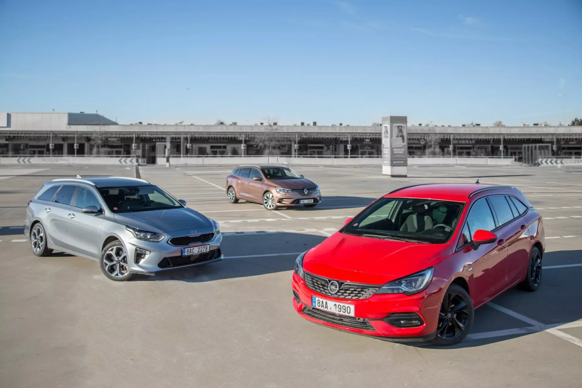 Tre modelli Kia Ceed del 2009 tra cui un hatchback rosso, un crossover dorato e una station wagon argento parcheggiati in un parcheggio in terrazza, fotografati da una posizione elevata per mostrare il design frontale, i profili laterali e la lunghezza dei veicoli