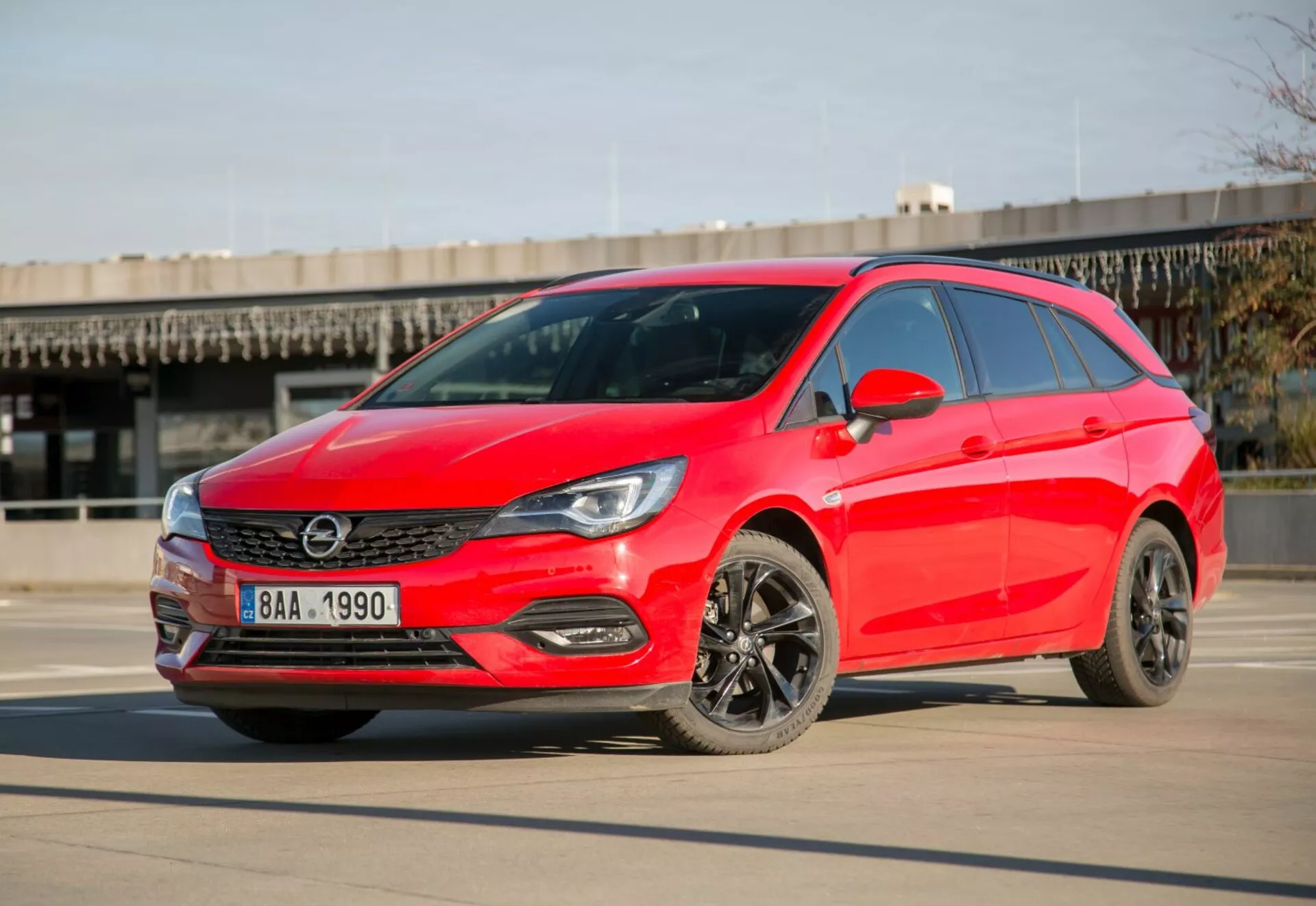 Hatchback rosso brillante Kia Ceed del 2009 parcheggiata su superficie in cemento liscio sotto cieli sereni, mostrando fari LED, griglia elegante, cerchi in lega scuri e design aerodinamico moderno da un angolo frontale di tre quarti durante il giorno.