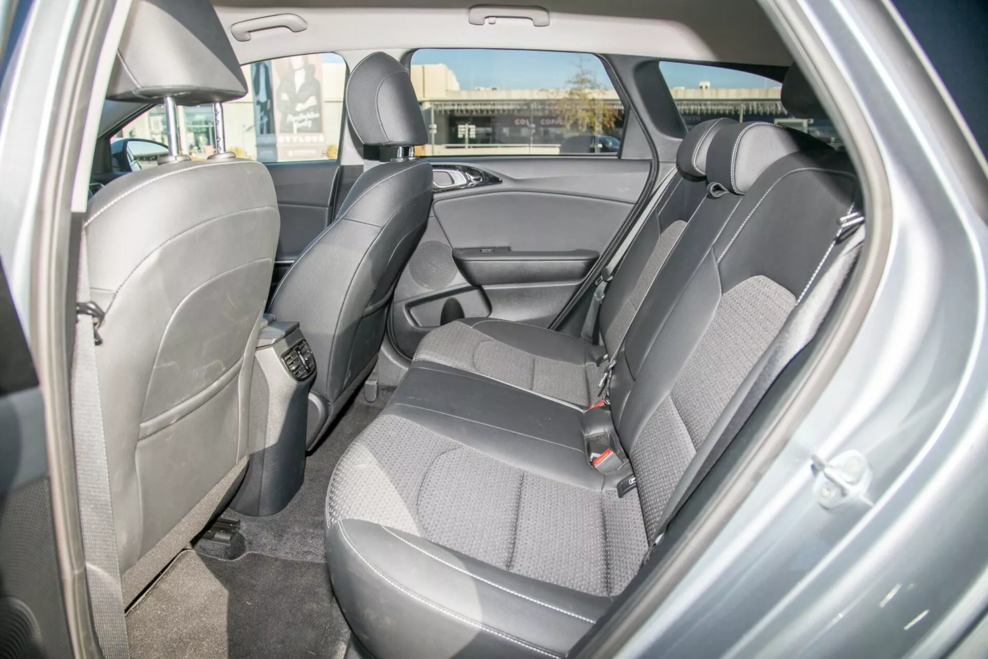 Vista interna di una Kia Cee'd 2009 che mostra il design e le caratteristiche della zona dei sedili posteriori, evidenziando rivestimenti in tessuto durevole a due toni, cinture di sicurezza visibili, poggiatesta regolabili, pannello porta con vano portaoggetti, possibili ancoraggi per seggiolini per bambini, pavimento rivestito in moquette e illuminazione ambiente a cupola dalla prospettiva della porta posteriore lato destro.