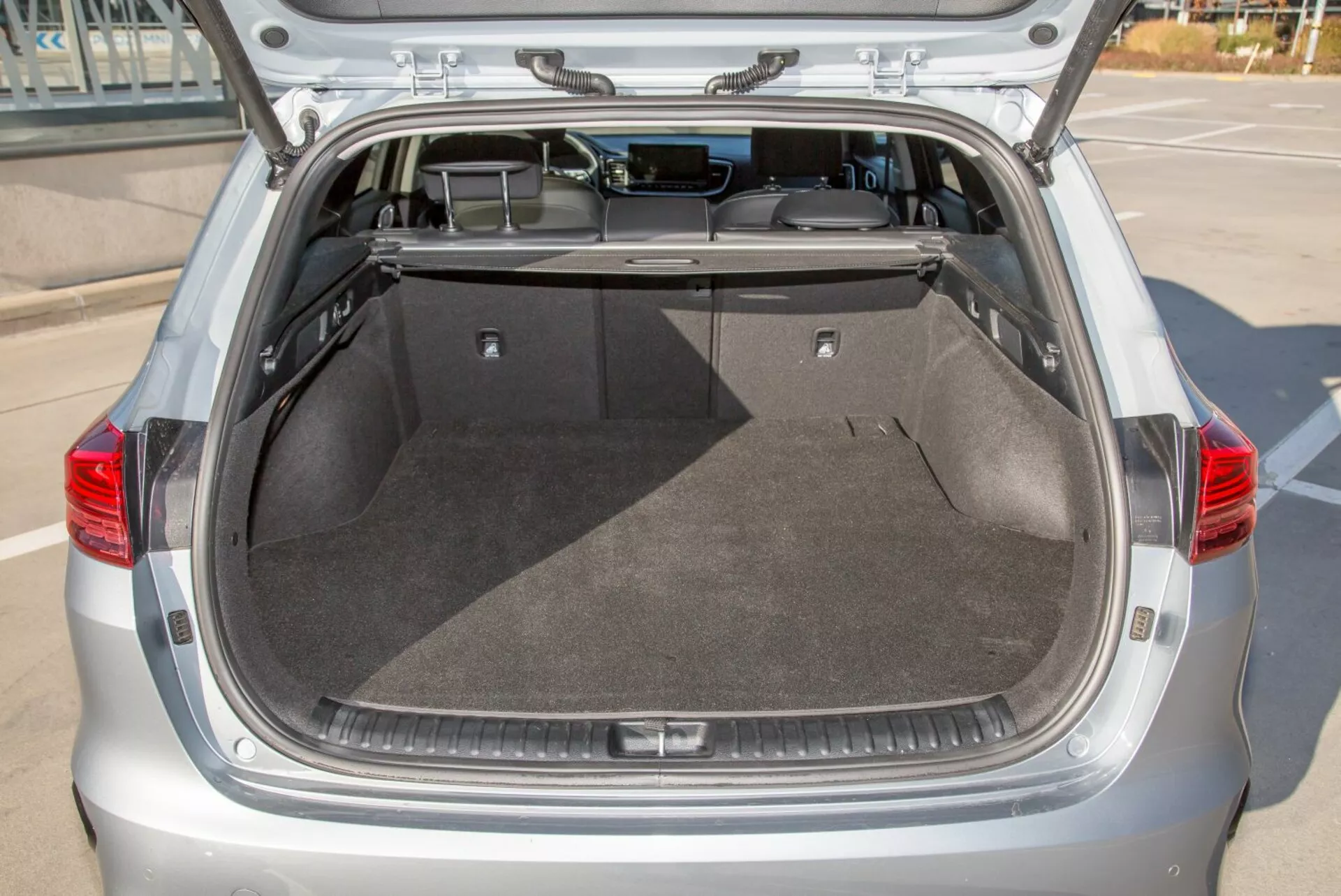 Compartimento bagagliaio posteriore di una hatchback Kia Cee'd 2009 con portellone aperto, che mostra ampio spazio di carico pulito, moquette, copertura retrattile e potenziale illuminazione interna