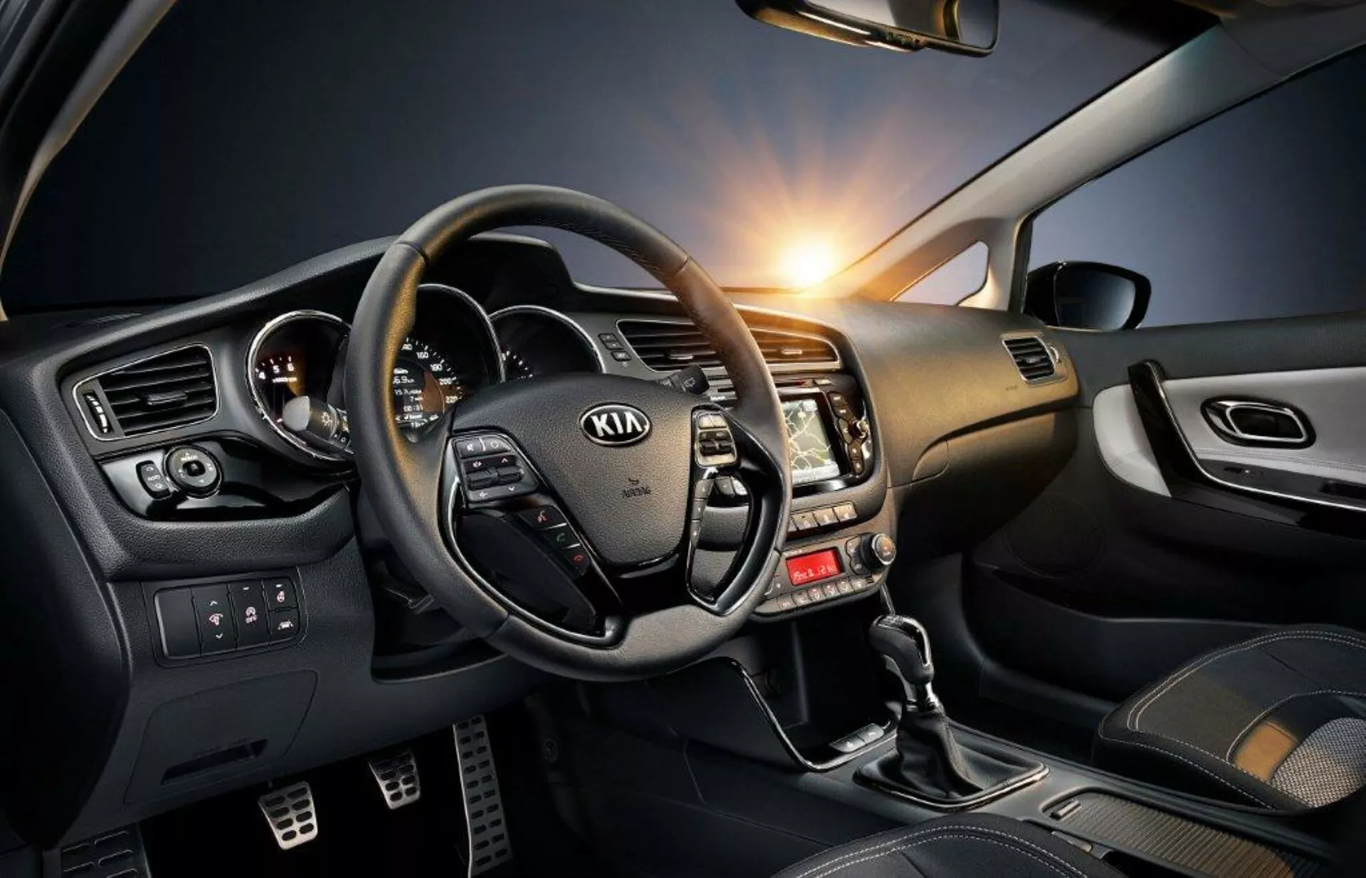 Vista dell'abitacolo di una Kia Ceed 2009 che mostra il volante con comandi integrati, il cruscotto con accenti metallici e il lato guidatore ricco di tecnologia, incluse la leva del cambio, i controlli dei finestrini elettrici e l'illuminazione ambientale.