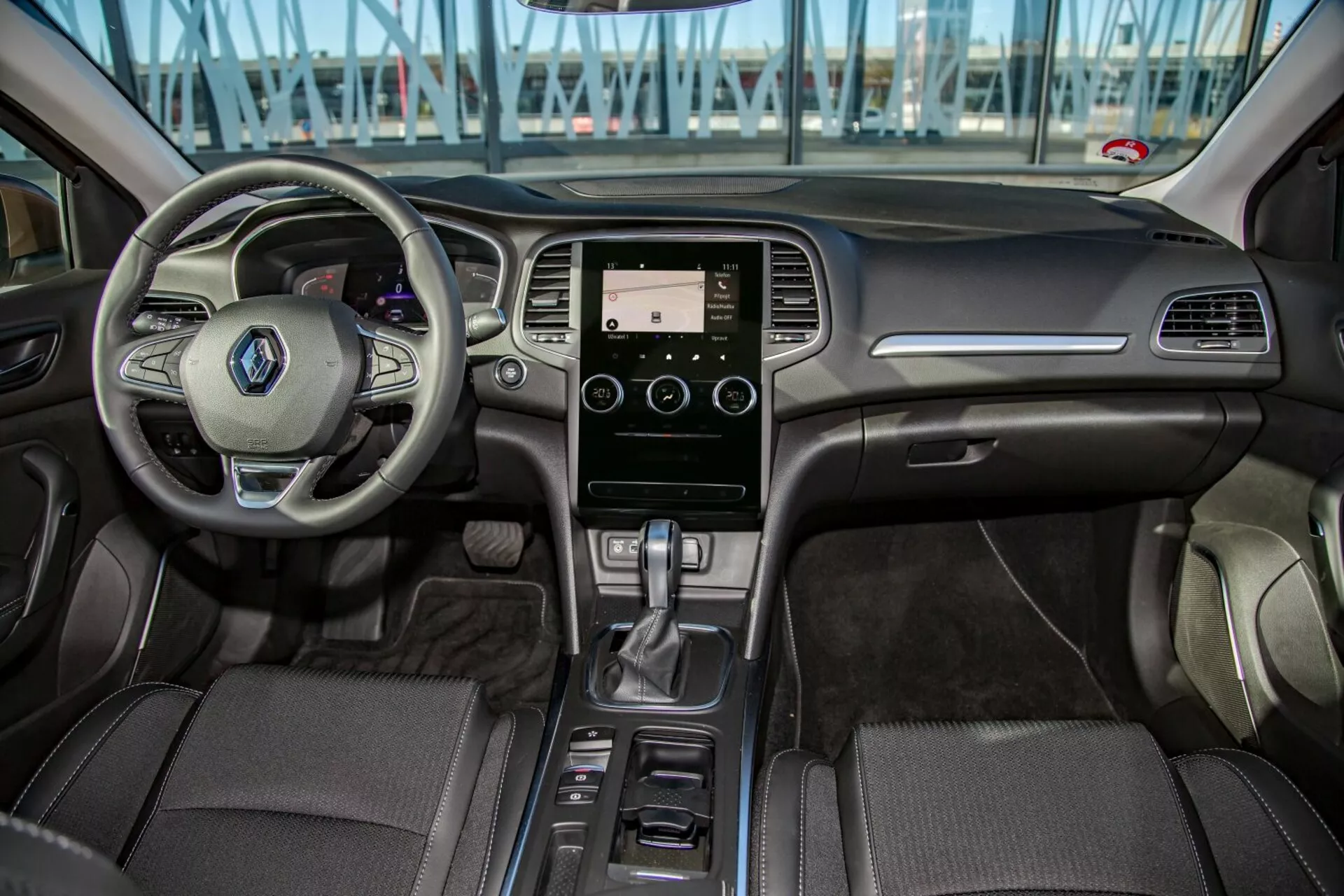 Vista interna della Kia Cee'd 2009 dal sedile posteriore mostrando volante multifunzione, sistema di infotainment touchscreen, leva del cambio automatica e tappezzeria dettagliata nell'area del cockpit anteriore