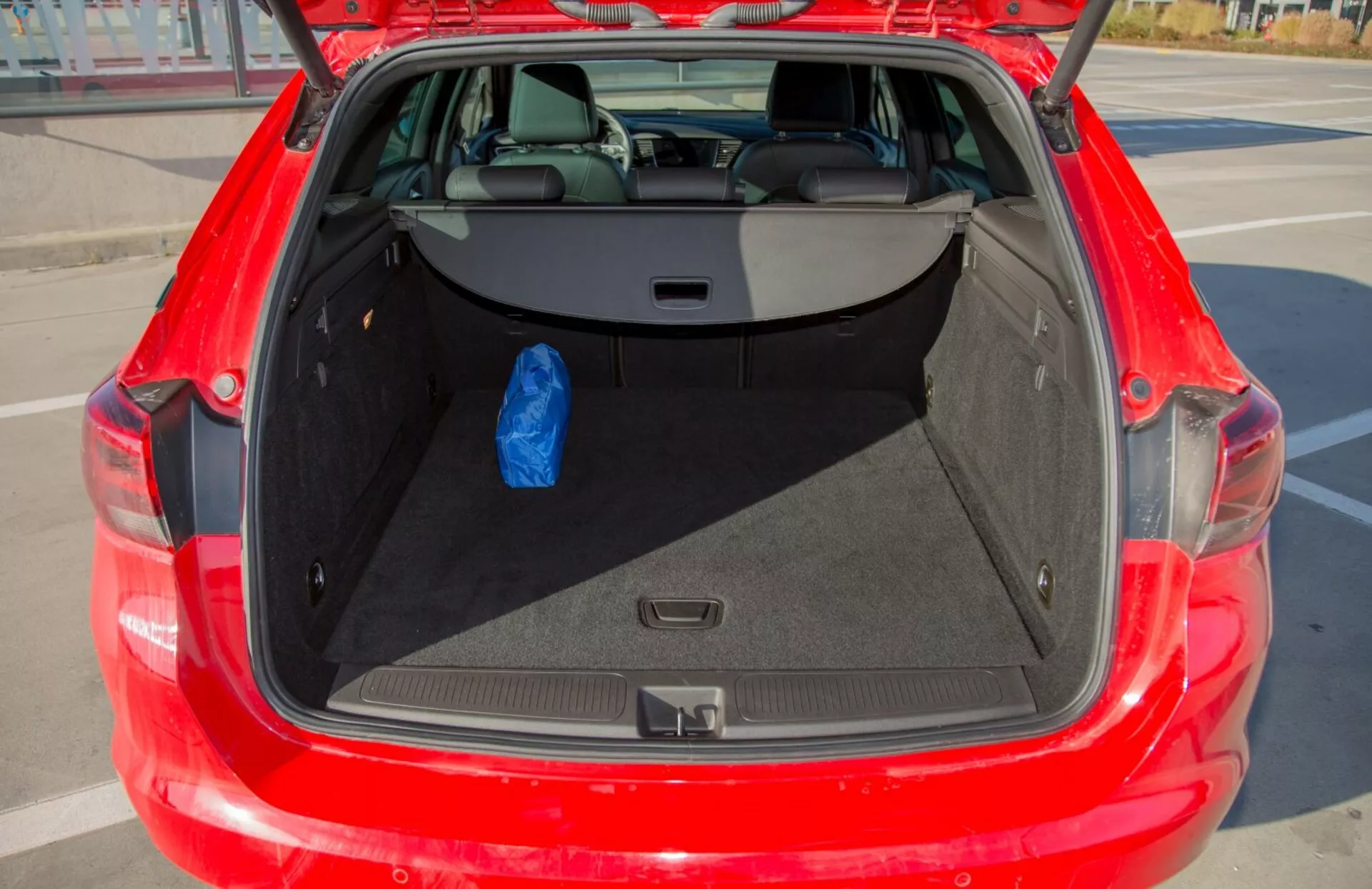 Vista dettagliata del bagagliaio aperto di una Kia Cee'd rossa del 2009, che mostra l'ampio spazio di stoccaggio e i sedili posteriori reclinabili 60/40, con una borsa blu che dimostra la sua utilità.