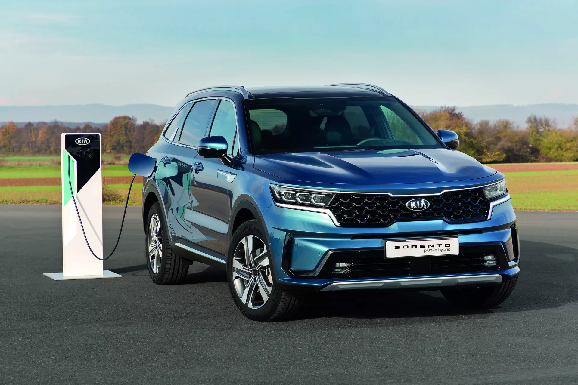 SUV Kia Sorento 2020 blu con fari LED e tecnologia plug-in ibrida, parcheggiata all'aperto con una stazione di ricarica alla luce del giorno che mostra design e capacità ecocompatibili