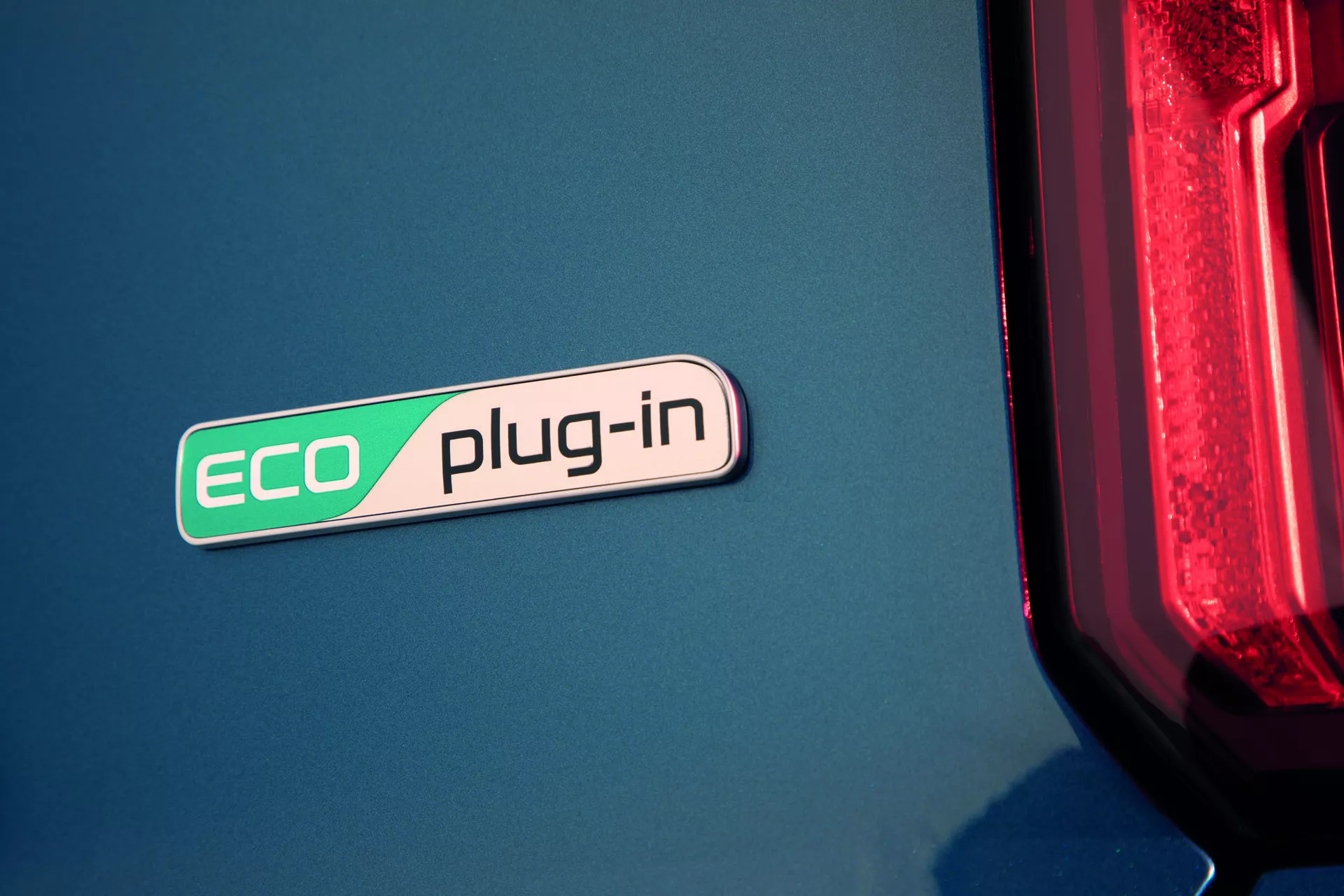 Primo piano del badge ECO plug-in della Kia Sorento 2020 (MQ4) che evidenzia la tecnologia ibrida su una carrozzeria blu con un accenno di moderno fanale posteriore LED