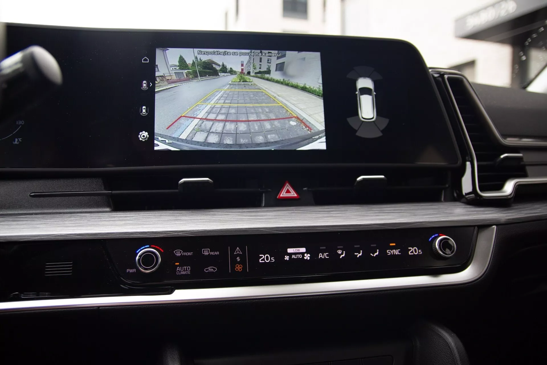 Vista interna della Kia Sportage 2022 dal sedile del conducente che evidenzia il touchscreen dell’infotainment con output della telecamera posteriore, pannello di controllo del clima e design esteticamente gradevole con accenti cromati e finiture lucide