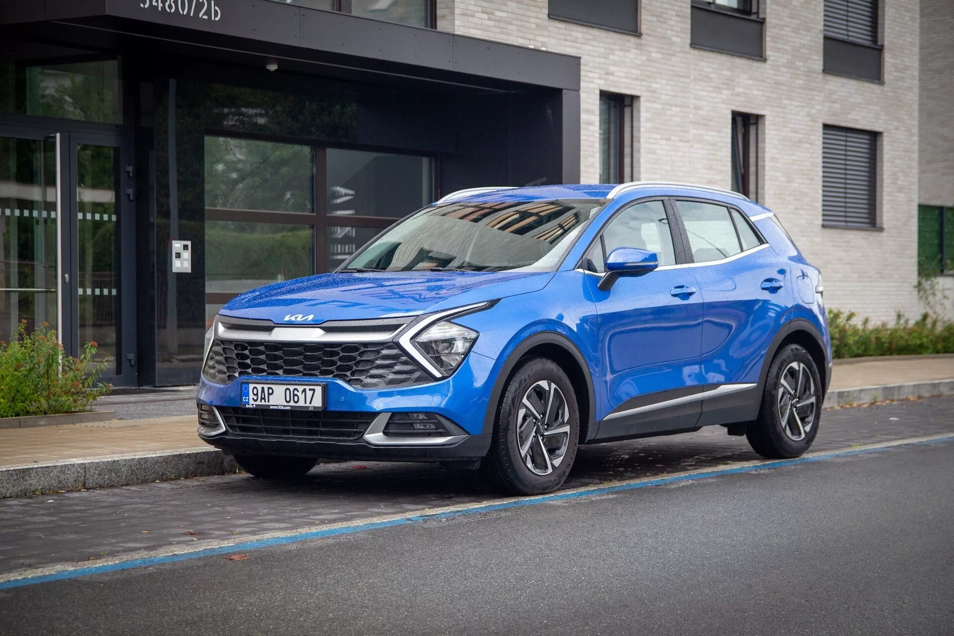 Kia Sportage 2022 blu, con vista frontale a tre quarti su strada urbana, evidenzia la sua alta guida, fari LED, cerchi in lega e tecnologia di sicurezza moderna.