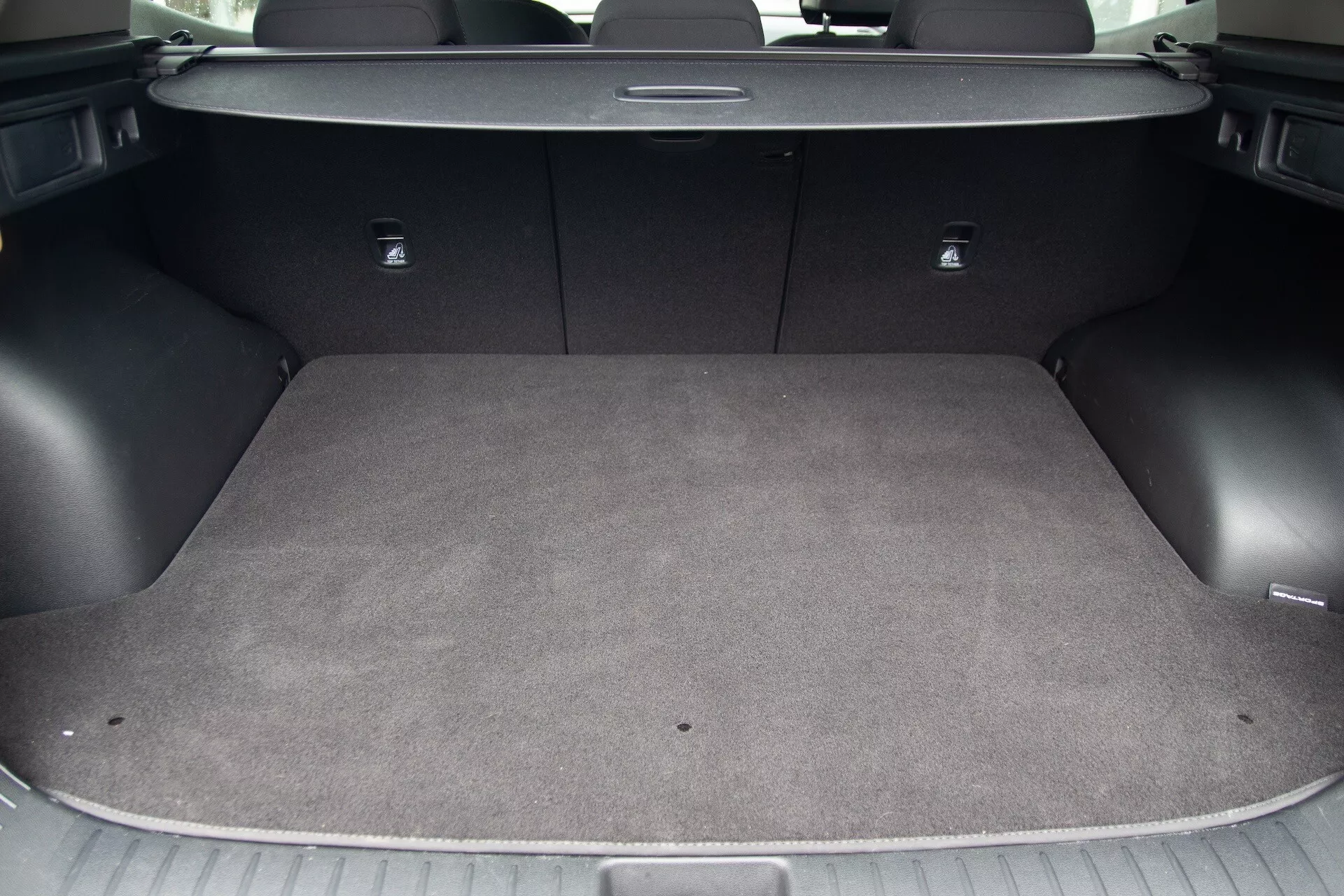 Vista dell'area di carico della Kia Sportage 2022 che mostra l'interno moquette, superficie di carico piatta, ganci di ancoraggio incorporati, punti di ancoraggio per seggiolini per bambini con sistema LATCH e sedili posteriori abbattibili 60/40 per uno spazio di carico flessibile