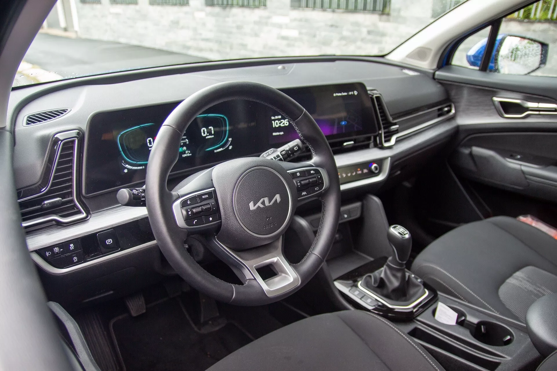 Interni della Kia Sportage 2022 con volante con pulsanti di controllo, cruscotto digitale e schermo infotainment
