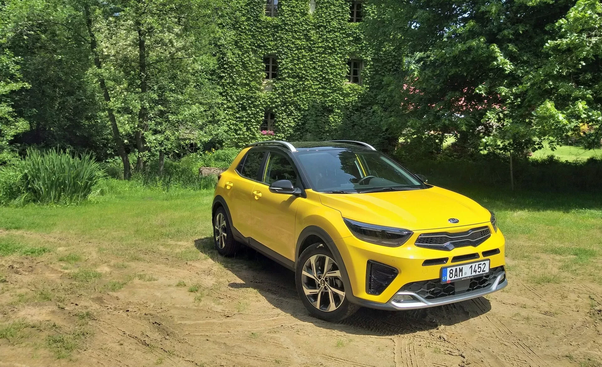SUV crossover giallo vibrante Kia Stonic 2017 in vista frontale da tre quarti che evidenzia la sua griglia anteriore, fari LED, cofano e lato conducente, impostato su uno sfondo naturale con luce solare su terreno libero, mostrando capacità fuoristrada, cerchi in lega sportivi e elementi di design moderno.