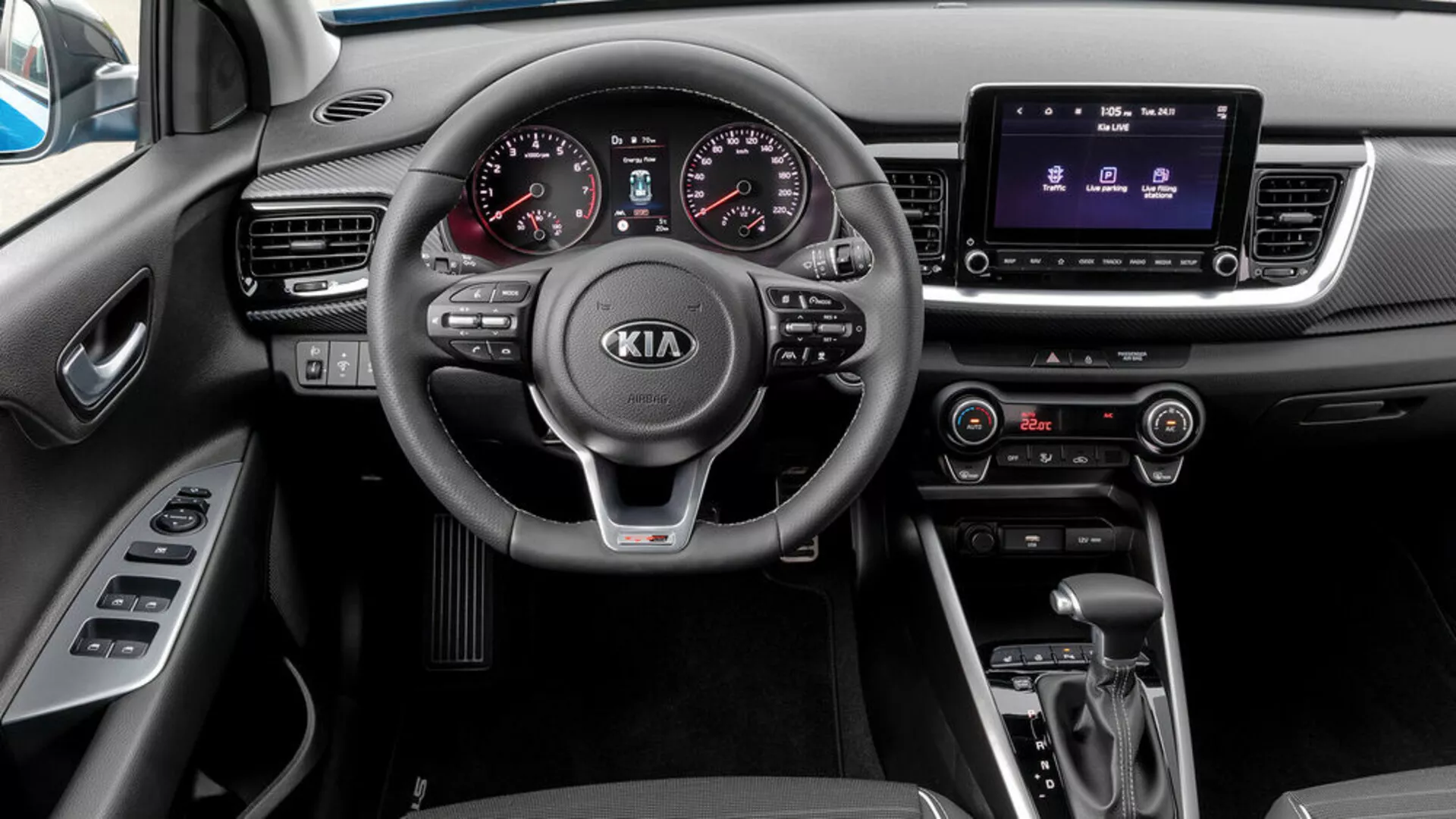 Vista interna di una Kia Stonic del 2017 dalla prospettiva del passeggero, dotata di volante a tre razze con comandi integrati, cruscotto analogico-digitale, sistema di infotainment touchscreen, controllo clima, trasmissione automatica e selettore modalità di guida.