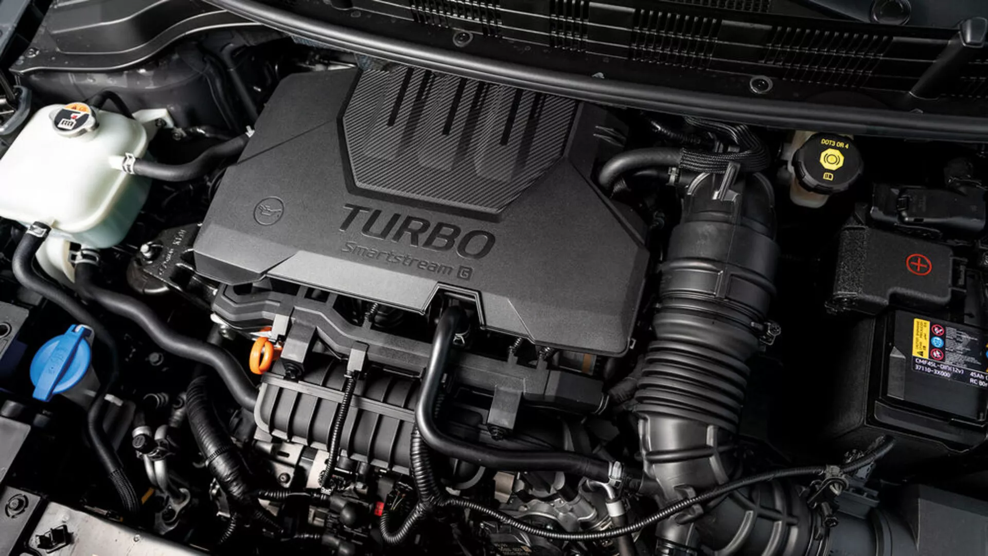 Vista ravvicinata del vano motore della Kia Stonic 2017 con copertura del motore turboalimentato e vari componenti meccanici visibili, mettendo in mostra gli aspetti tecnologici del veicolo