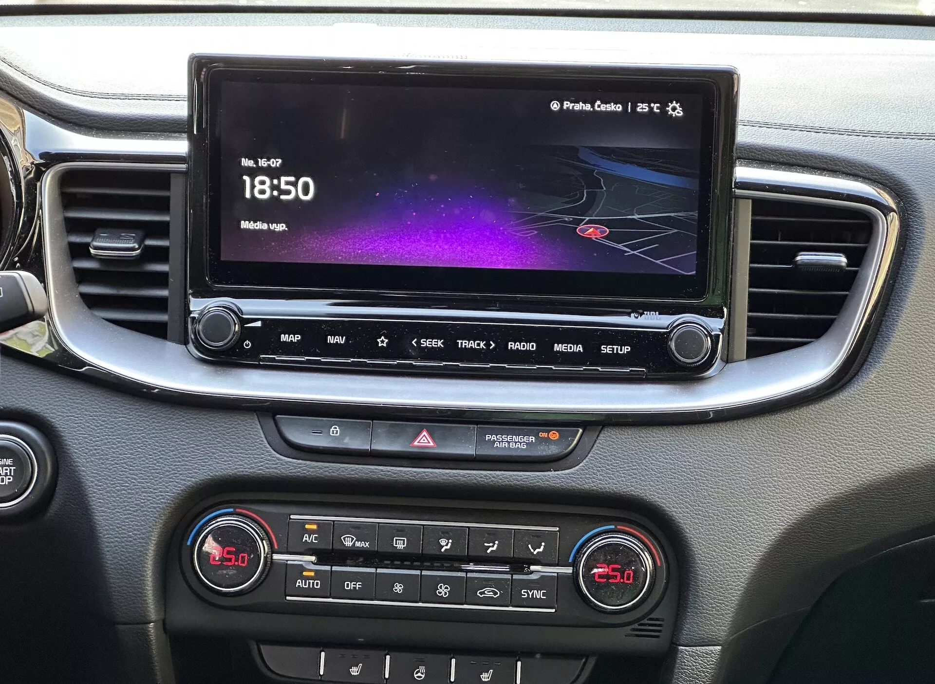 Vista dettagliata dell'interno della Kia Xceed 2022 che mostra la console centrale con un touchscreen per l'infotainment che visualizza un'interfaccia colorata con navigazione e informazioni sui media, una fila di pulsanti di accesso rapido, controllo delle luci di emergenza e un pannello di controllo climatico a doppia zona, il tutto incorniciato da una finitura argento.