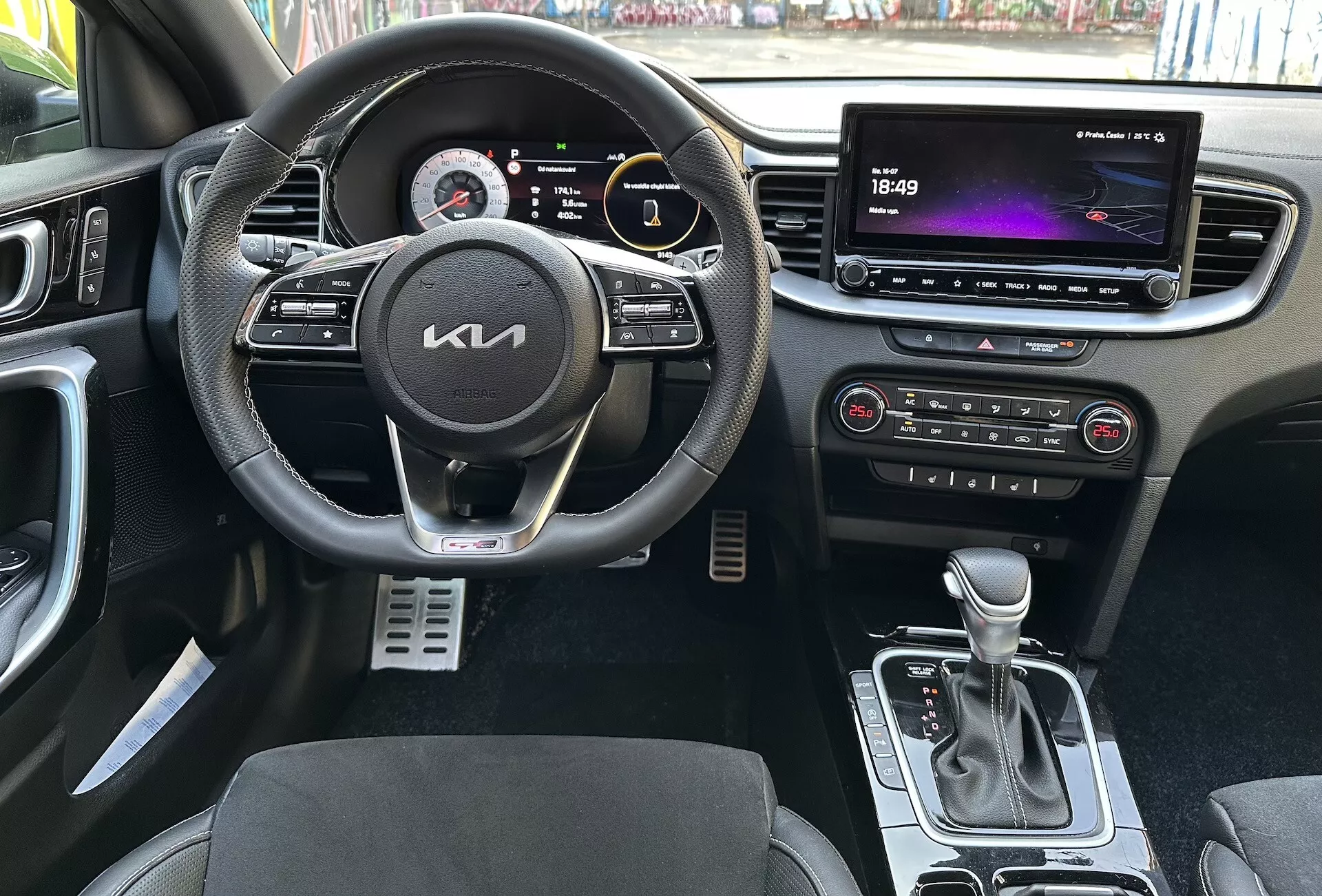 Vista interna del Kia XCeed 2022 che evidenzia le caratteristiche focalizzate sul conducente come un volante multifunzionale rivestito in pelle con pulsanti per multimedia e controllo crociera, un cluster strumenti digitale, un grande sistema di infotainment touchscreen, controlli automatici del clima, leva del cambio automatica, sedili con tappezzeria bicolore e pedali sportivi in metallo da una prospettiva in prima persona.