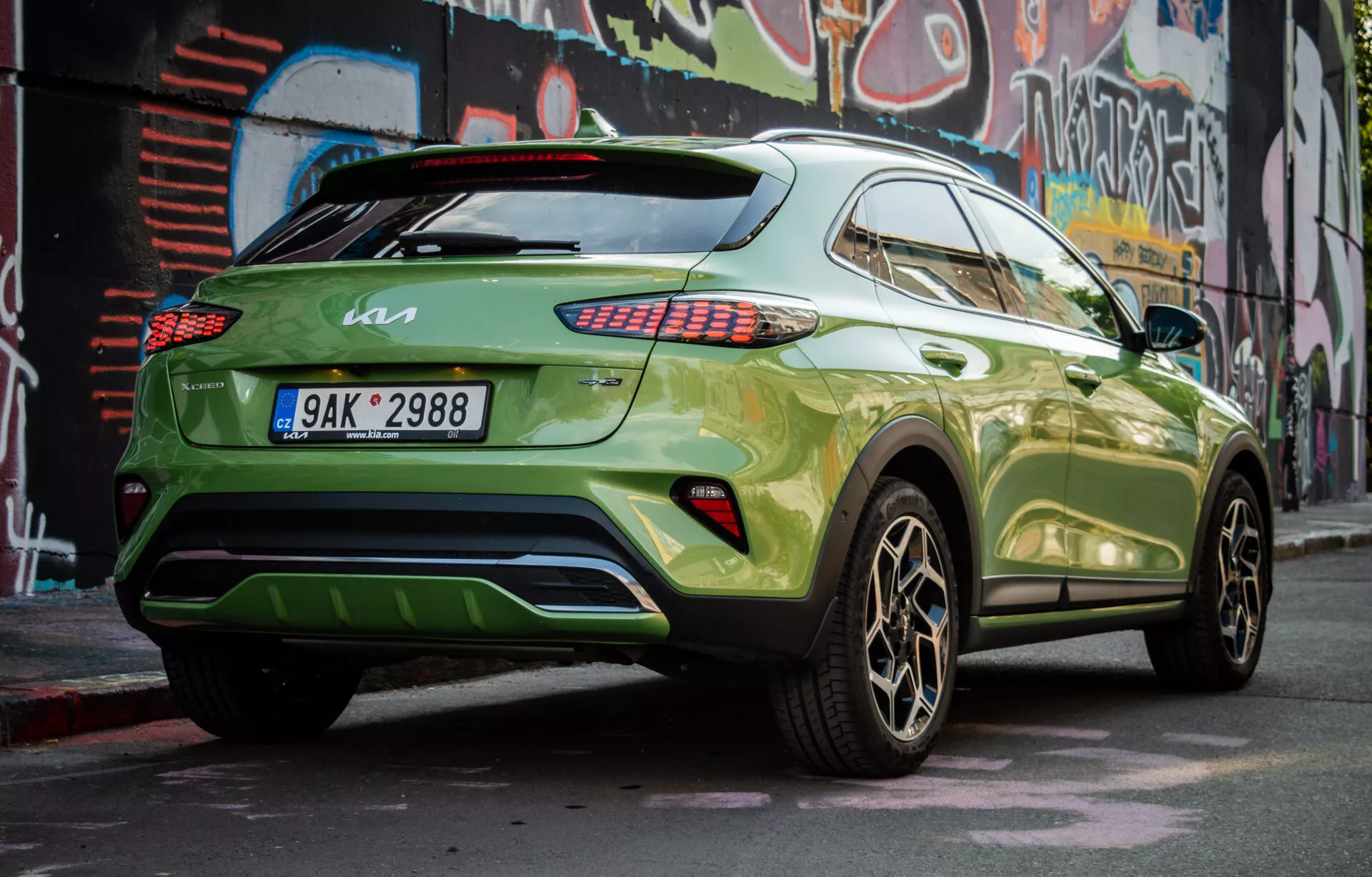 SUV crossover moderno Kia XCeed 2022 parcheggiato in diagonale mostrando il suo quarto posteriore destro, con vernice verde vibrante e cerchi in lega scura, dimostrando il profilo laterale del veicolo, il design posteriore, i fanali posteriori LED, i vetri oscurati, uno spoiler sul tetto e un potenziale diffusore posteriore