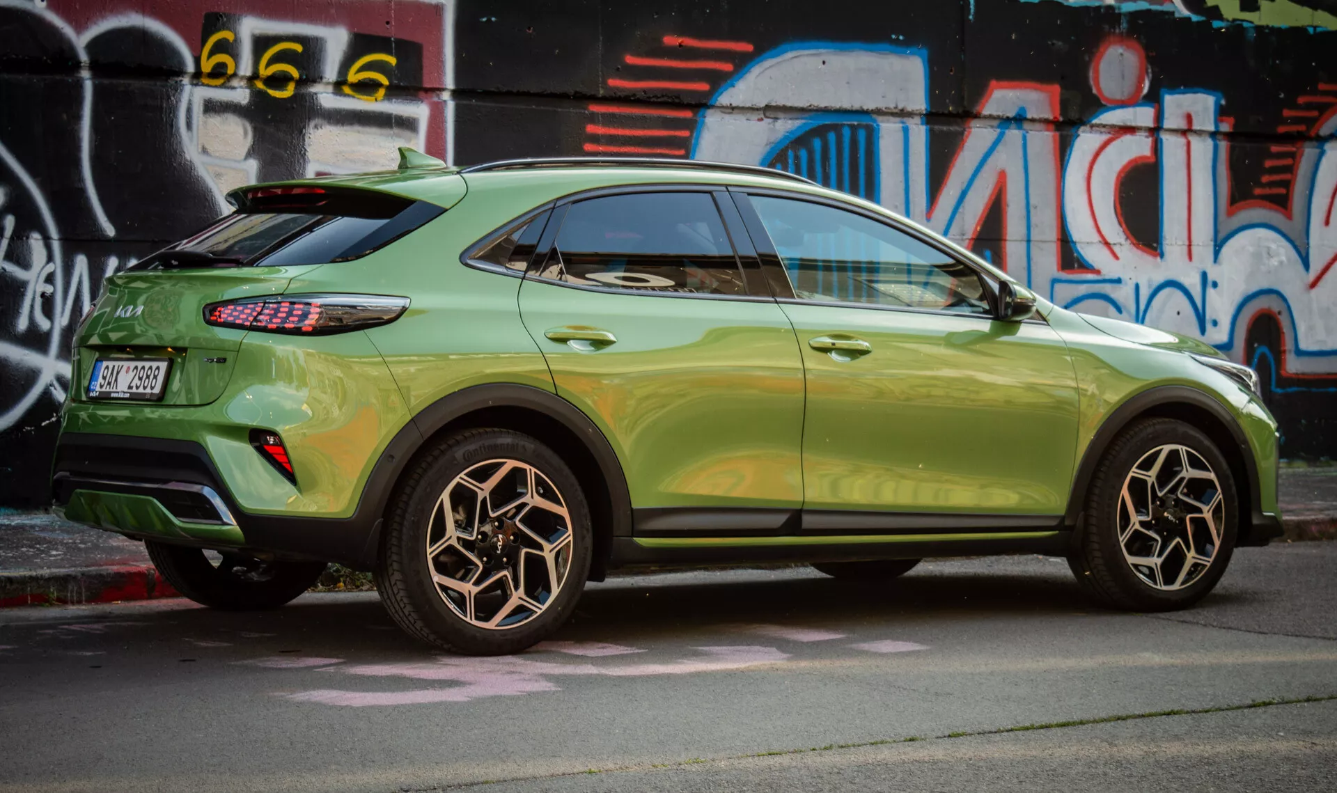 Vista laterale della Kia XCeed 2022 che evidenzia il design della ruota posteriore, vernice metallica verde, luci posteriori a LED e stile SUV compatto con caratteristiche aerodinamiche su uno sfondo di arte di strada urbana.