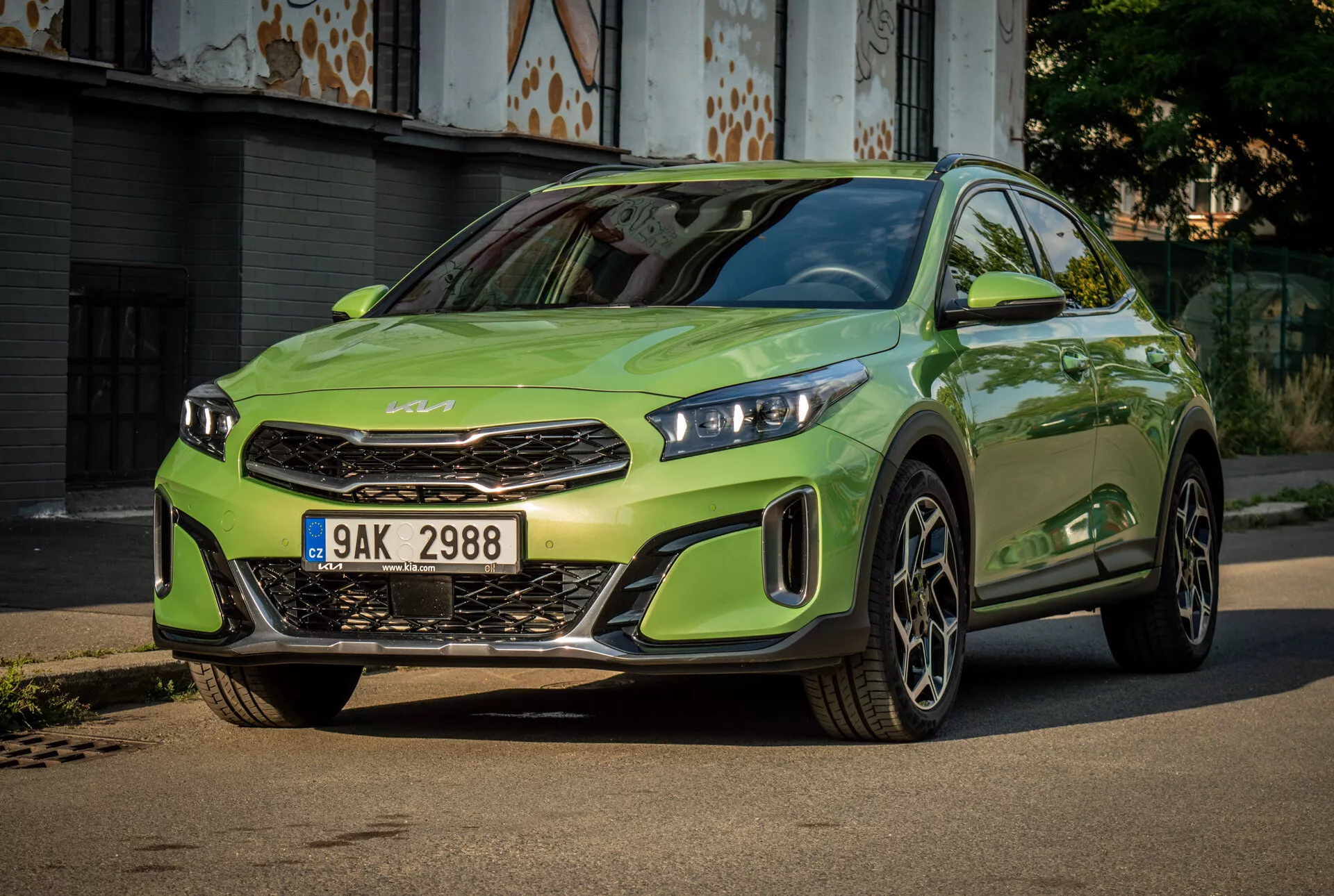 Kia XCeed 2022 in un vivace verde lime dotata di fari LED, griglia frontale prominente con emblema del marchio, paraurti anteriore sportivo e grandi ruote in lega, centrata su una strada asfaltata con uno sfondo urbano