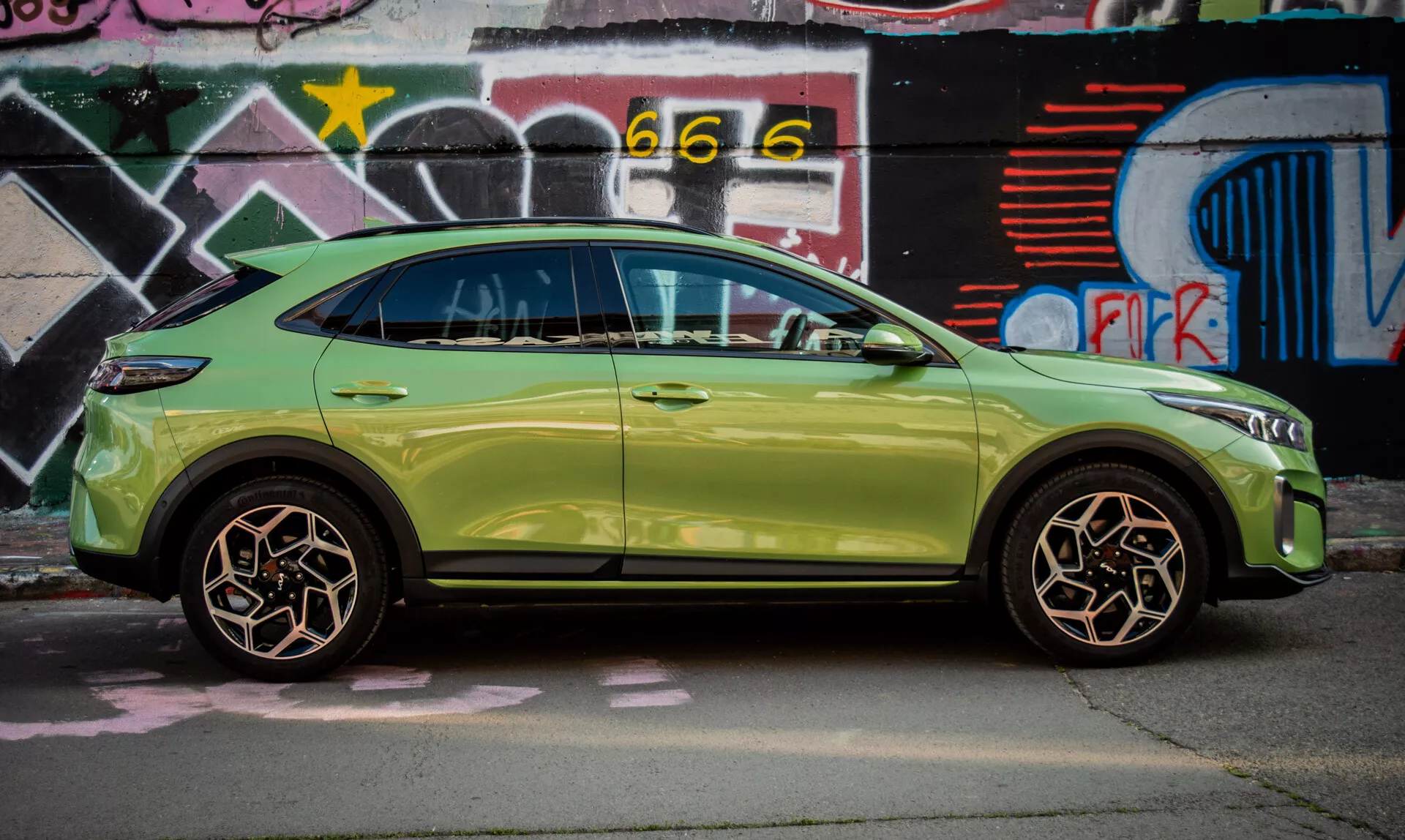 SUV compatto Kia XCeed del 2022 in verde lime parcheggiato accanto a un muro coperto di graffiti, mostrando il suo design elegante e funzioni avanzate come l'entrata senza chiave e indicatori di direzione integrati negli specchietti laterali.