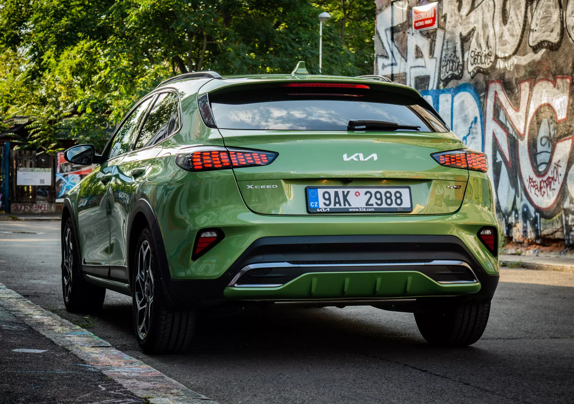 Vista posteriore di un crossover/SUV Kia XCeed verde 2022 che mostra il marchio, il design dei fari posteriori LED, la posizione della targa, l'estetica del paraurti inferiore e la finitura lucida su una strada urbana.
