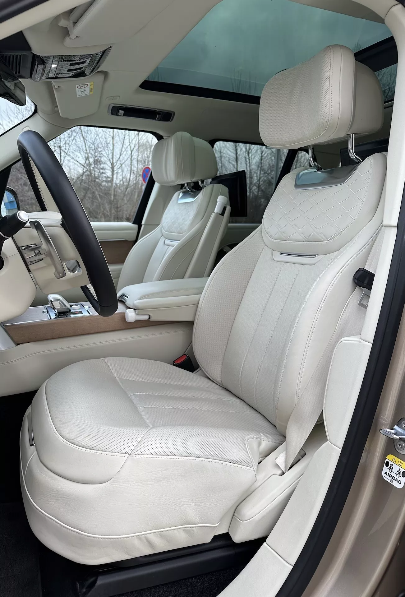 Vista interna del Land Rover Range Rover 2021 che evidenzia il lato del conducente con sedili in pelle crema di lusso, volante multifunzione, e elementi di controllo avanzati sulla console centrale