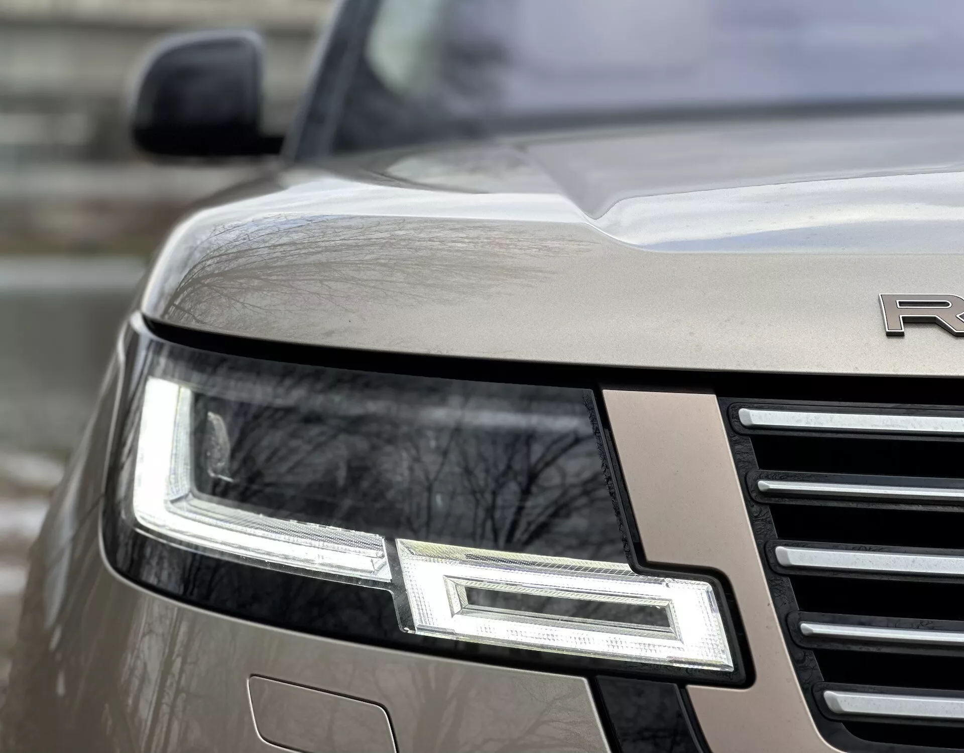 Vista ravvicinata angolata dell'angolo anteriore della Land Rover Range Rover 2021 che evidenzia l'assemblaggio dei fari LED, la griglia cromata e l'emblema parziale su un corpo metallico