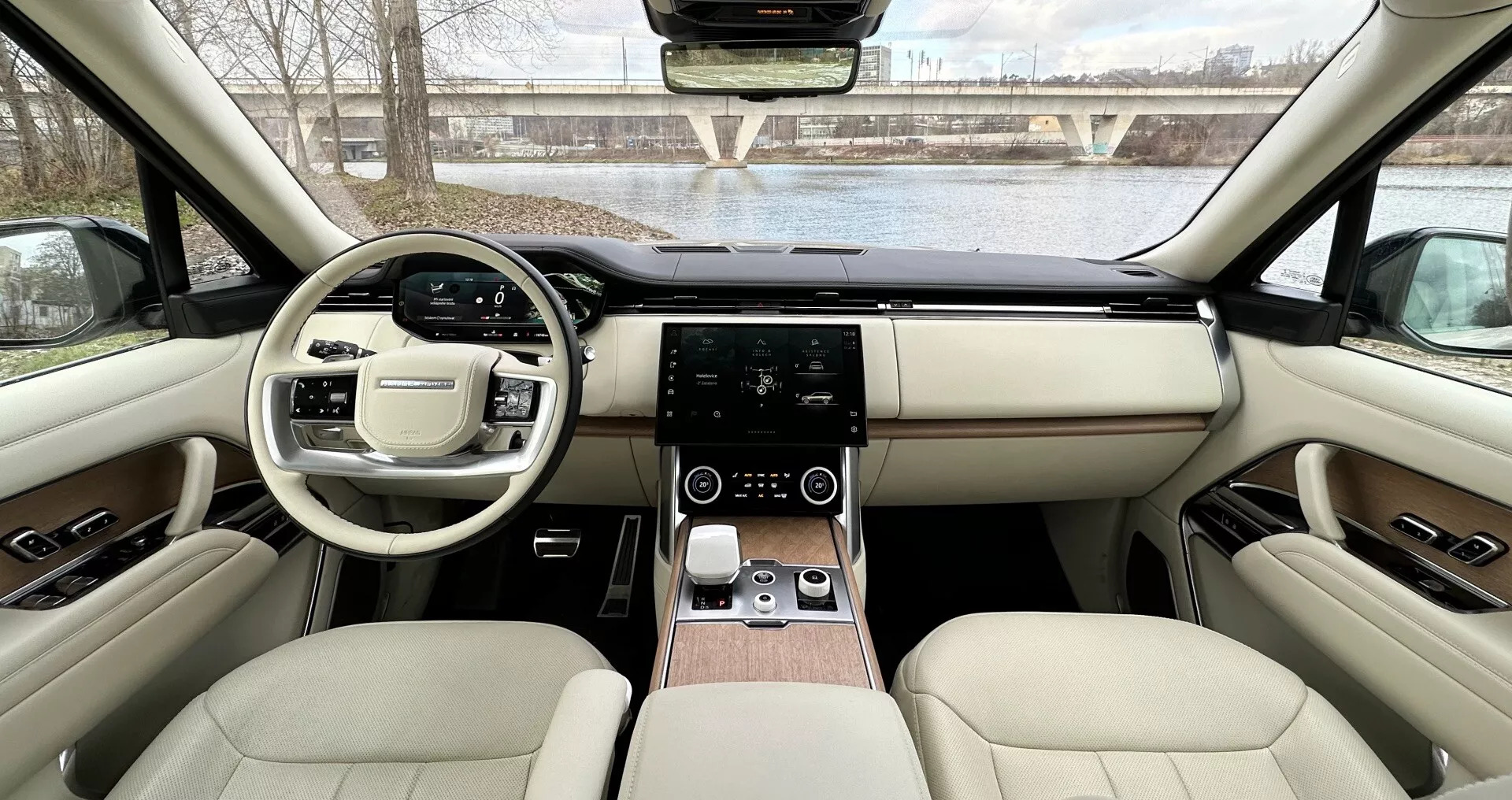 Vista interna della Land Rover Range Rover 2021 dai sedili posteriori verso il cruscotto che mostra design simmetrico, volante con pulsanti multifunzione, sistema di infotainment touch, controllo del clima digitale, tappezzeria in pelle di lusso con accenti in legno e caratteristiche tecnologiche avanzate