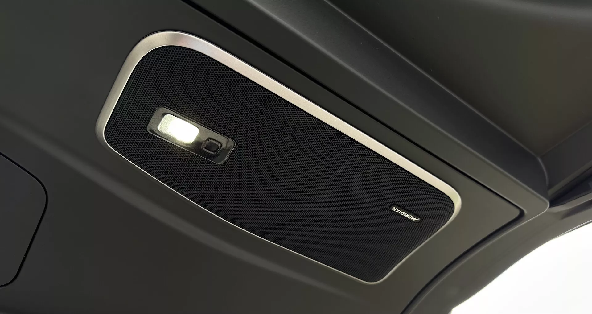 Vista ravvicinata della console superiore interna del Range Rover 2021, che mostra una griglia dell'altoparlante di alta qualità e luce a cupola, sottolineando l'acustica premium della cabina e la tecnologia avanzata di illuminazione interna.