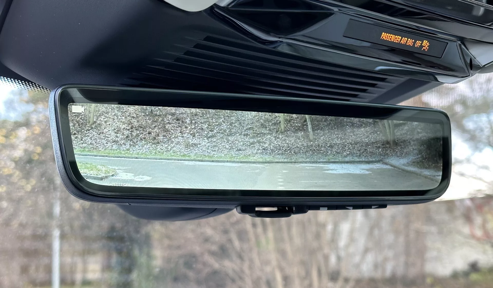 Vista ravvicinata dello specchietto retrovisore auto-oscurante elettrocromico all'interno di un Range Rover 2021, evidenziando il suo design senza cornice, le caratteristiche della cabina interna e la scena riflessa dei dintorni esterni immobili