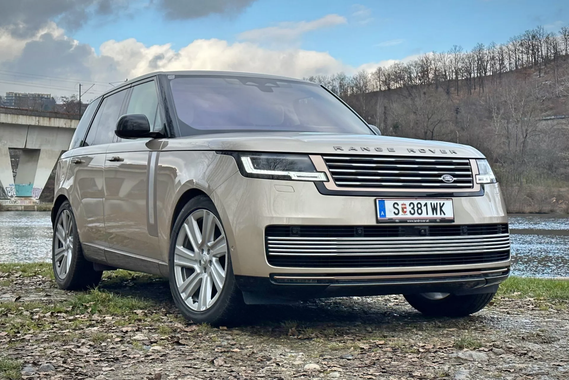 SUV di lusso Land Rover Range Rover 2021, vista frontale tre quarti che mette in evidenza la griglia cromata, fari LED, ruote in lega a più razze e design aerodinamico, parcheggiato all'aperto vicino a un fiume e un ponte