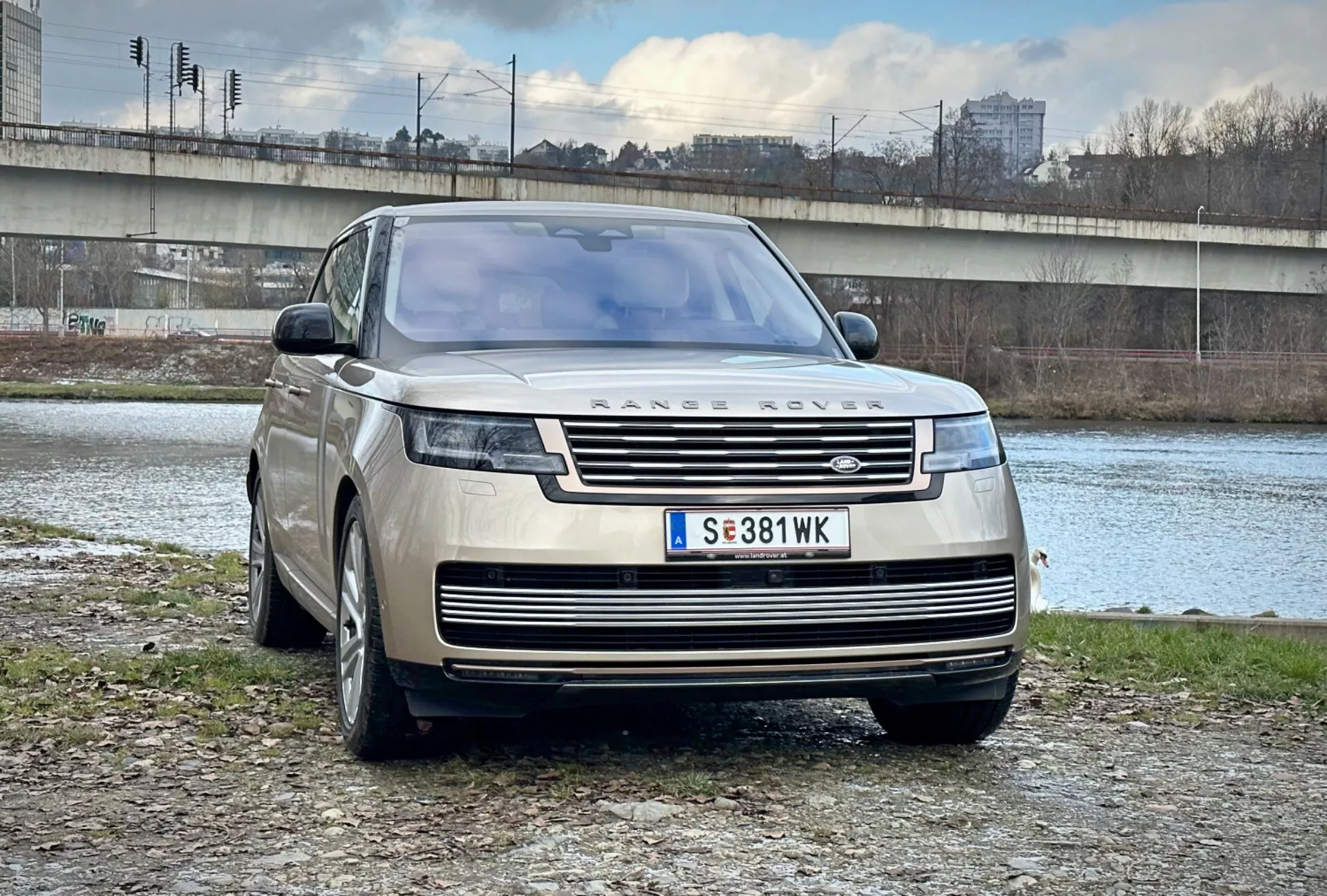 SUV di lusso Range Rover 2021 parcheggiato all'aperto vicino a un fiume e un ponte in un contesto urbano, che mostra il suo design moderno, la griglia frontale e i fari LED eleganti