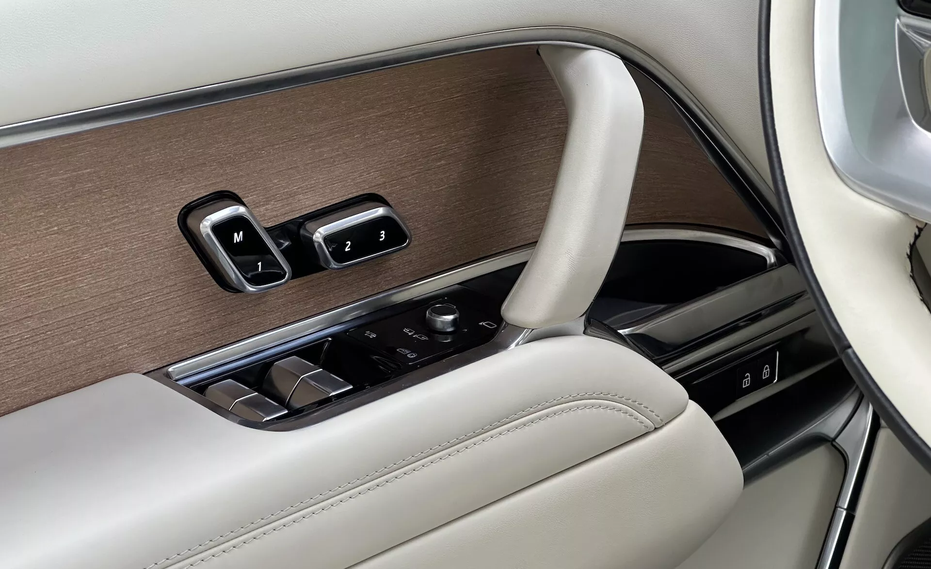 Dettaglio interno del Land Rover Range Rover 2021 che mostra il pannello porta lato guidatore con controlli finestre, regolazioni specchietti, impostazioni memoria sedile in un design lussuoso con finiture in legno, cromo e pelle, e una manopola di controllo per l'infotainment.