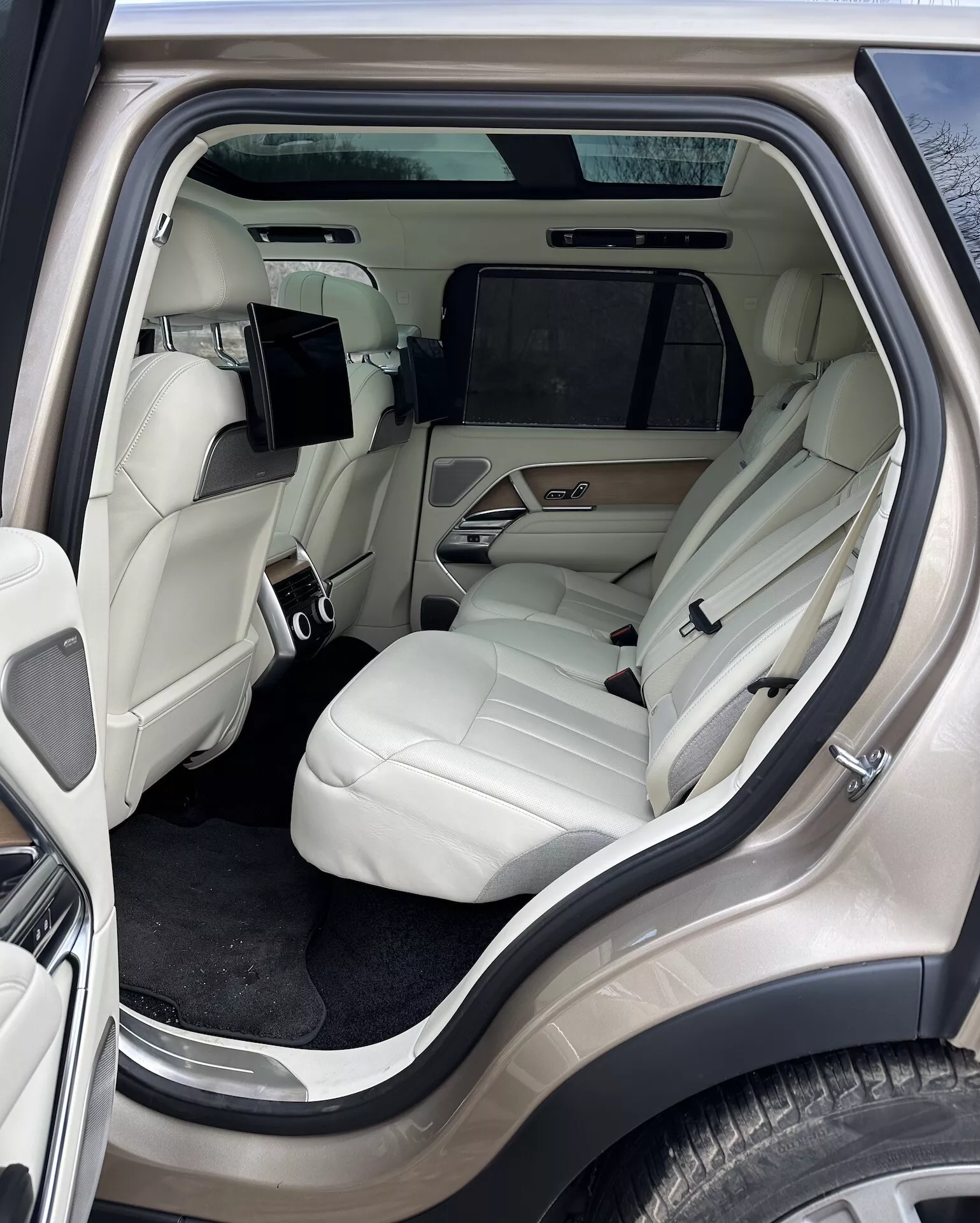 Vista interna del Land Rover Range Rover 2021 focalizzata sul lussuoso compartimento passeggeri posteriore da un angolo laterale esterno, caratterizzata da sedili in pelle di colore chiaro, console centrale avanzata, sistema di intrattenimento e dettagli di lusso