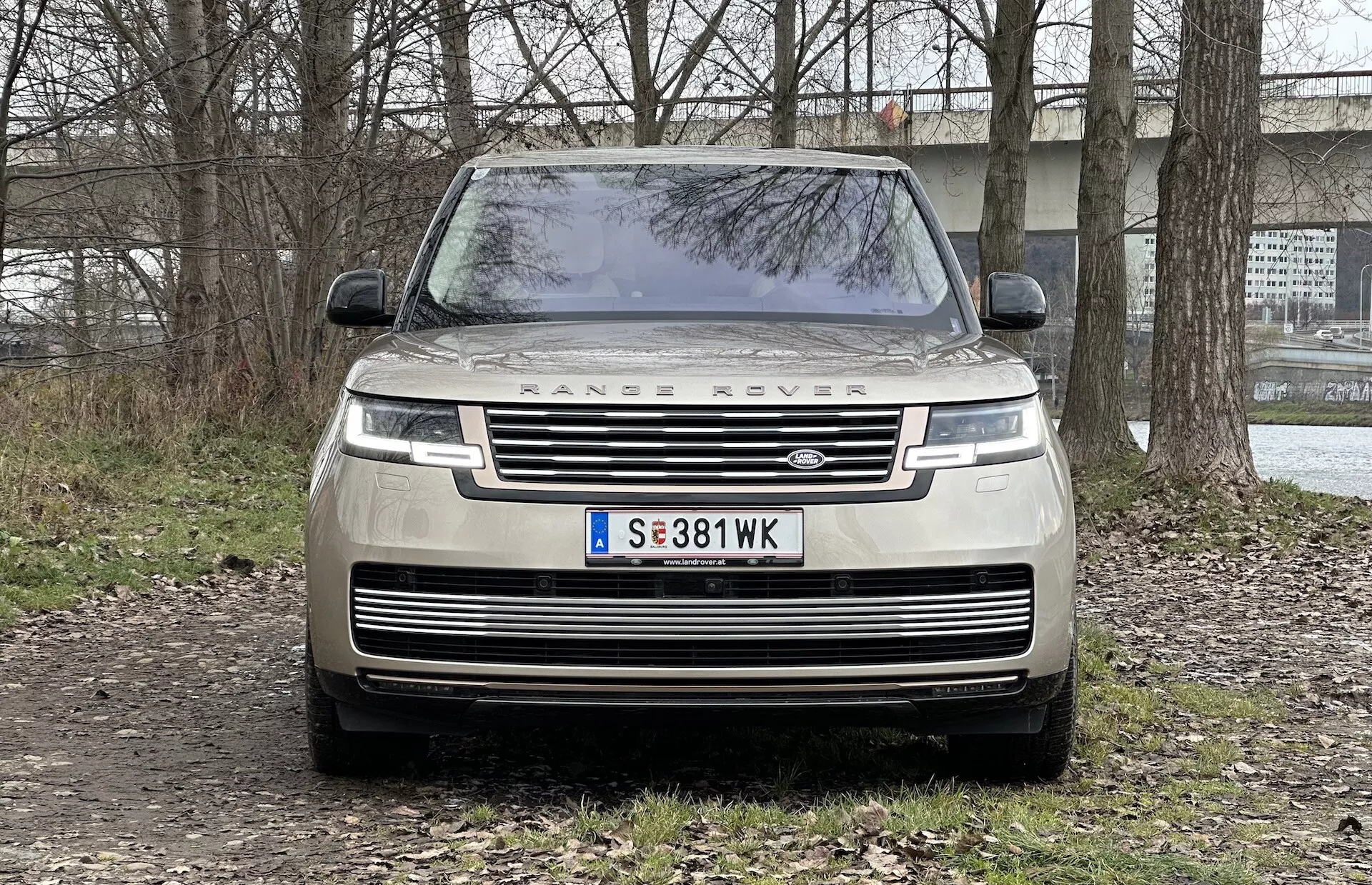 Vista frontale di un Range Rover 2021 che mostra la griglia, i fari LED, la scritta 'RANGE ROVER' sul cofano, parcheggiato su una superficie non asfaltata con uno sfondo semirurale
