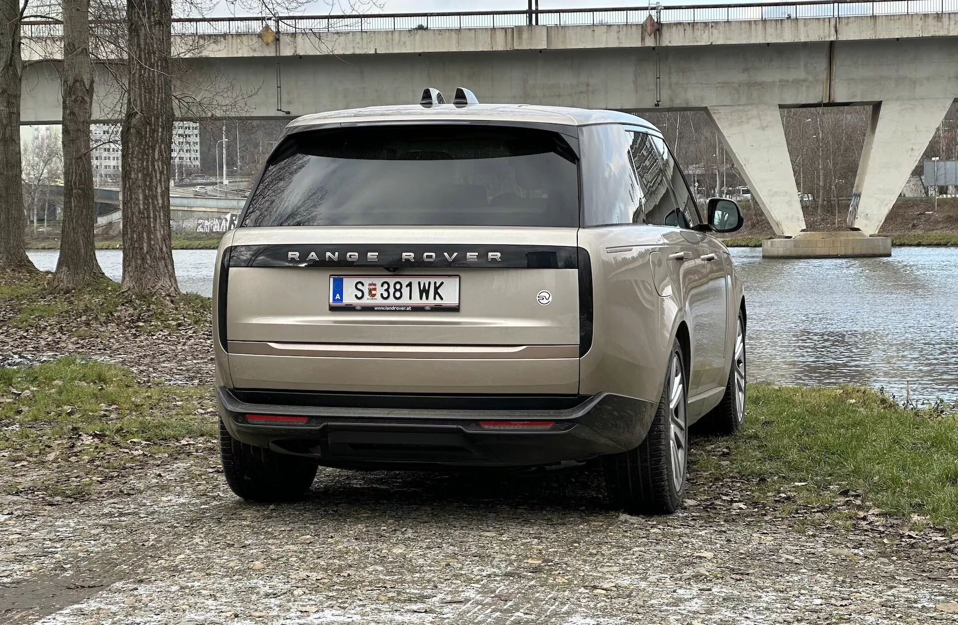 Vista posteriore di una Range Rover 2021 parcheggiata all'aperto con un corpo d'acqua e un ponte sullo sfondo, mostrando luci posteriori LED, doppio scarico, vetri oscurati e cerchi in lega a più razze.