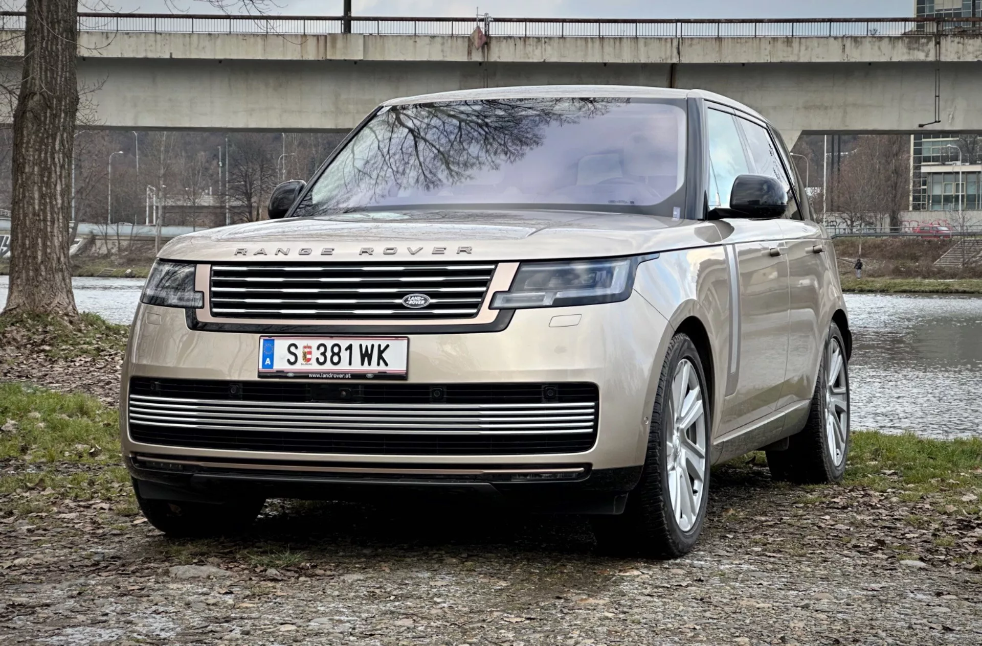 Range Rover 2021 in una straordinaria vista frontale a tre quarti che mette in mostra la sua griglia distintiva, i fari LED eleganti e la robusta piastra di protezione anteriore su uno sfondo di parco urbano, sottolineando lusso e capacità fuoristrada.