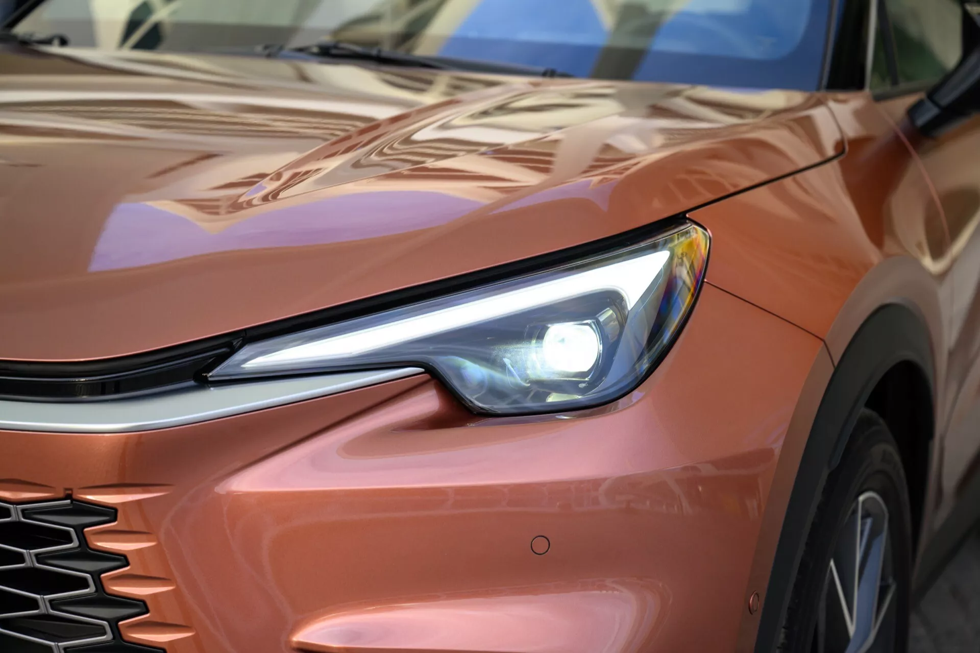 Immagine ravvicinata di una Lexus LBX 2024, prima generazione, concentrata sul quarto anteriore sinistro con vista dettagliata del faro LED, della griglia e del cofano e parafango contornati da un angolo basso, enfatizzando il suo design elegante e gli elementi tecnologici moderni.