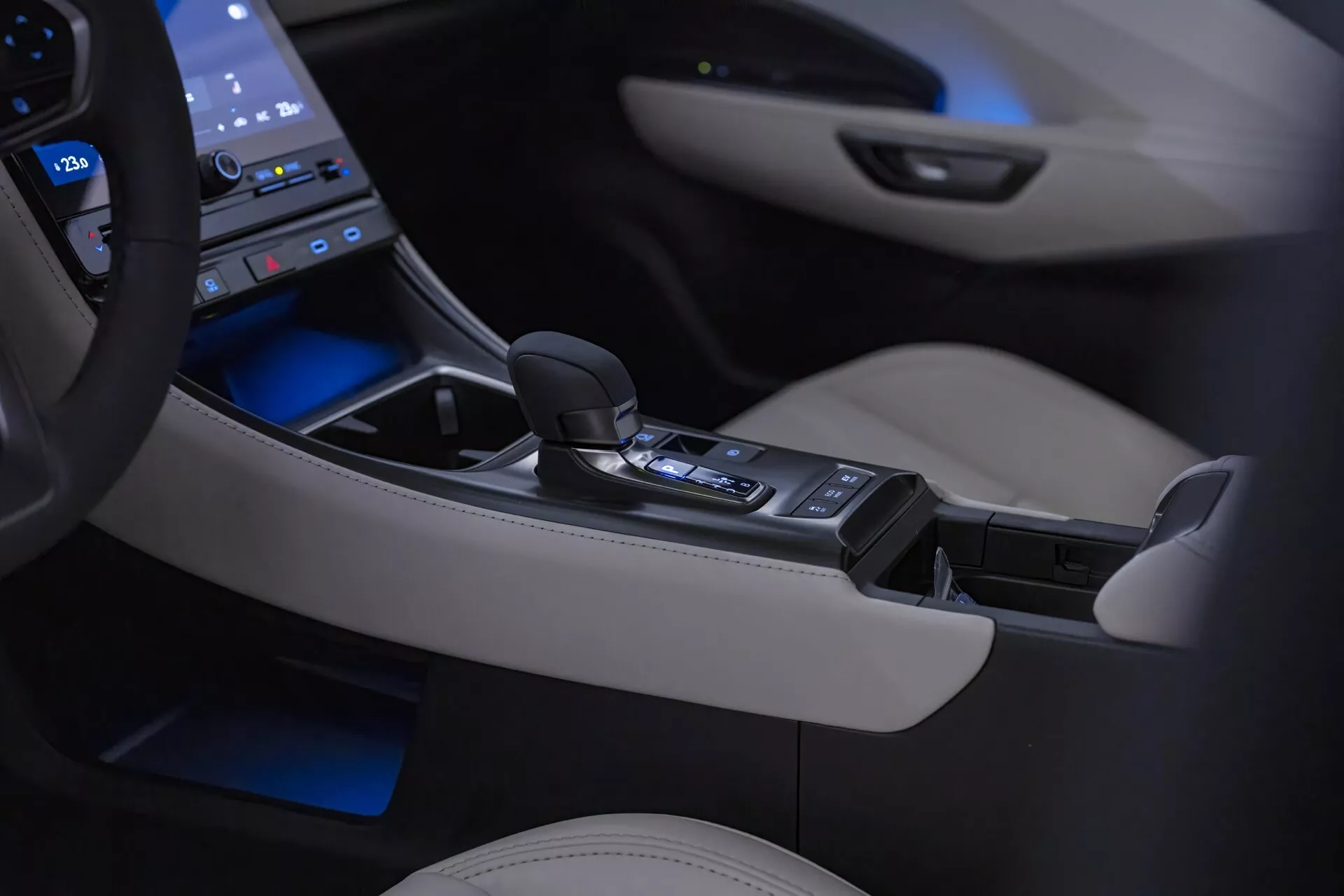 Interno del Lexus LBX 1ª Generazione 2024 che mostra la consolle centrale e la leva del cambio automatico con illuminazione ambientale, circondata da un pannello touch high-tech e dettagli in pelle crema di lusso
