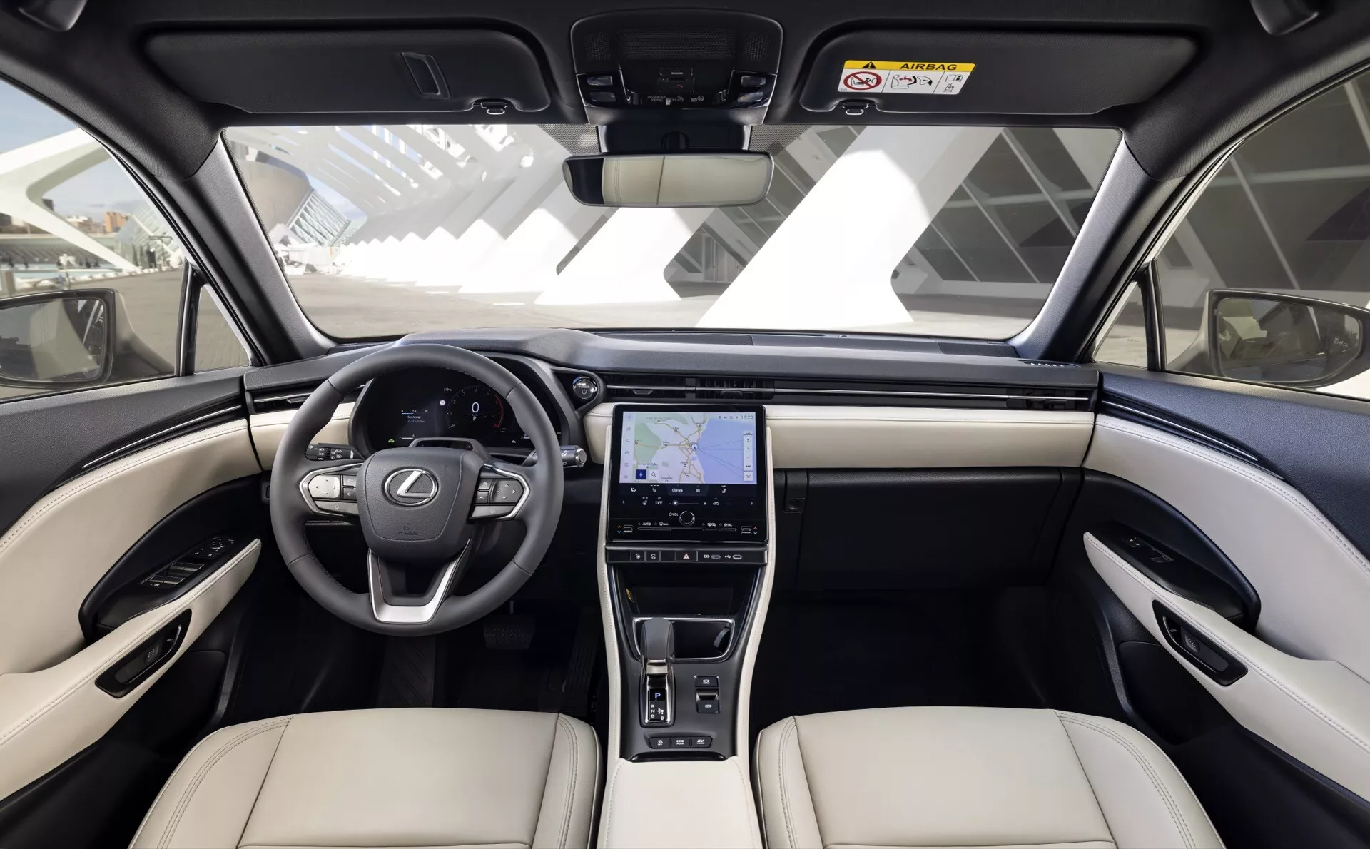 Vista frontale-centrale dell'interno della Lexus LBX 2024 con cruscotto bicolore, volante multifunzione a tre razze, grande display infotainment con GPS e sedili premium beige