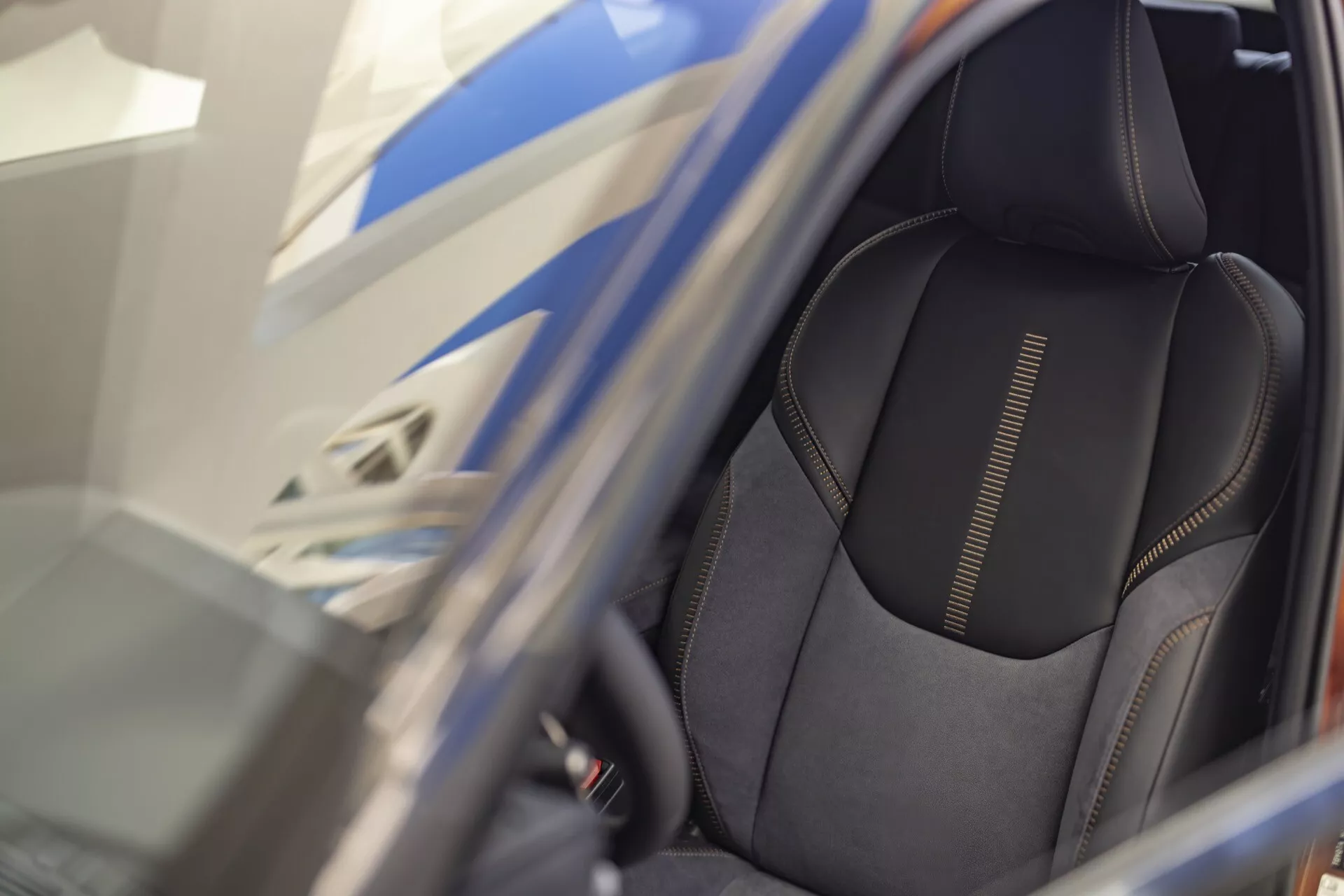 Primo piano del sedile del conducente della 1ª generazione Lexus LBX 2024 mostrando tappezzeria in materiale scuro di alta qualità con cuciture dettagliate e design di supporto laterale sportivo, visto attraverso una porta aperta con focus su caratteristiche ergonomiche e possibili comandi di regolazione del sedile elettrico.