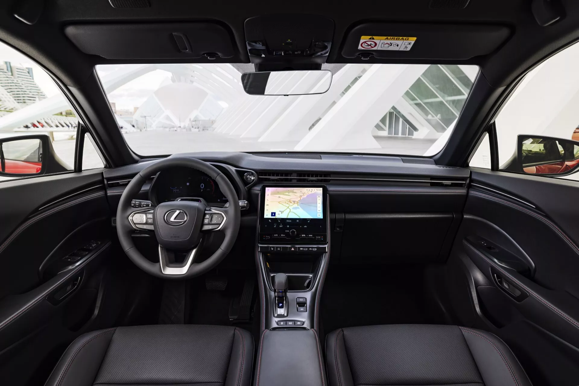 Vista interna della Lexus LBX di 1ª generazione 2024 dal sedile posteriore centrale che mostra cruscotto, volante, sedili anteriori in pelle e funzionalità di alta tecnologia