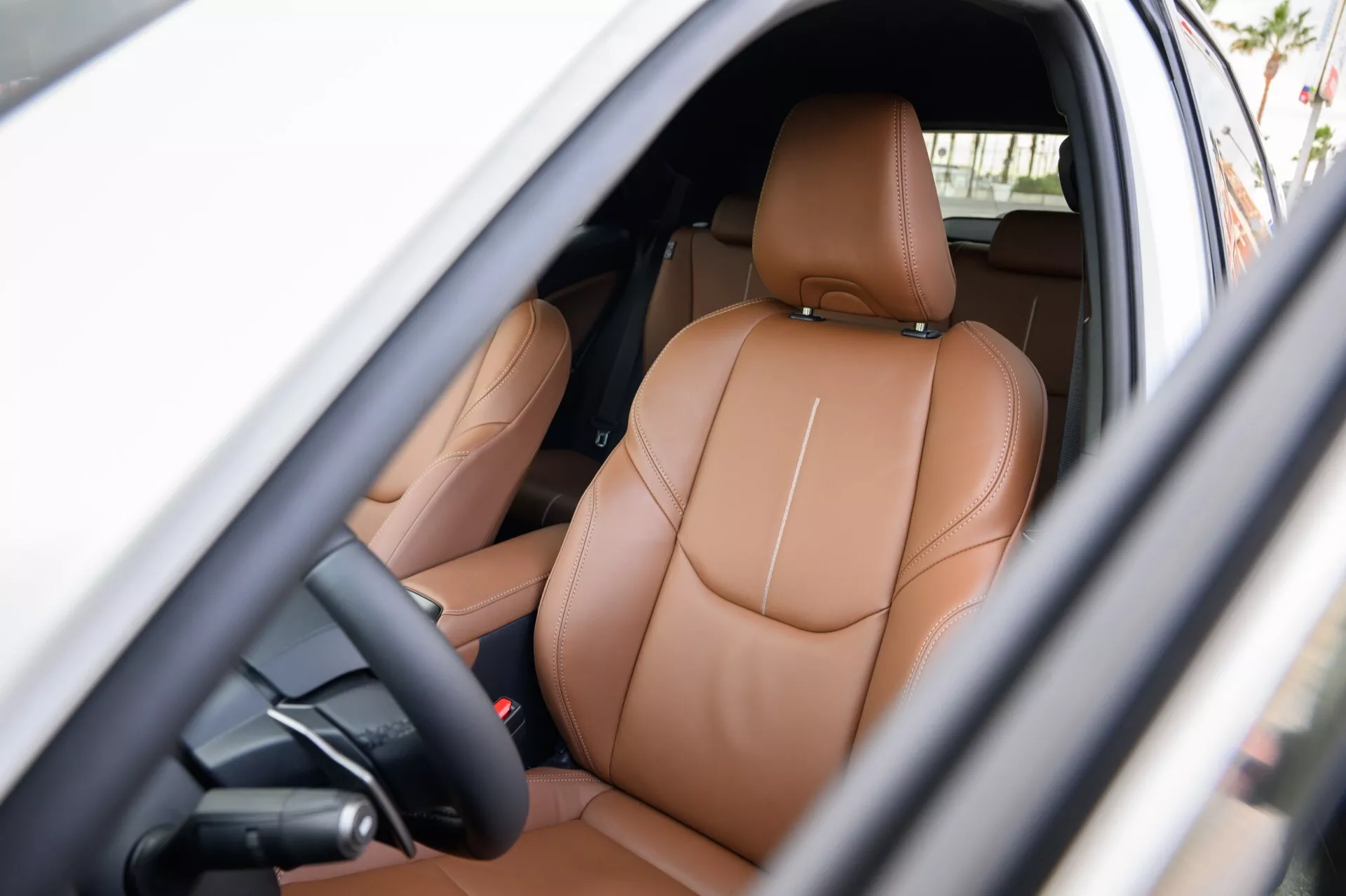 Vista interna di una Lexus LBX 2024 di 1ª Generazione che mostra l'area del guidatore con sedili in pelle marrone chiaro di lusso, comandi per la regolazione elettrica e accenni di funzionalità high-tech visibili attraverso la porta aperta sul lato del guidatore