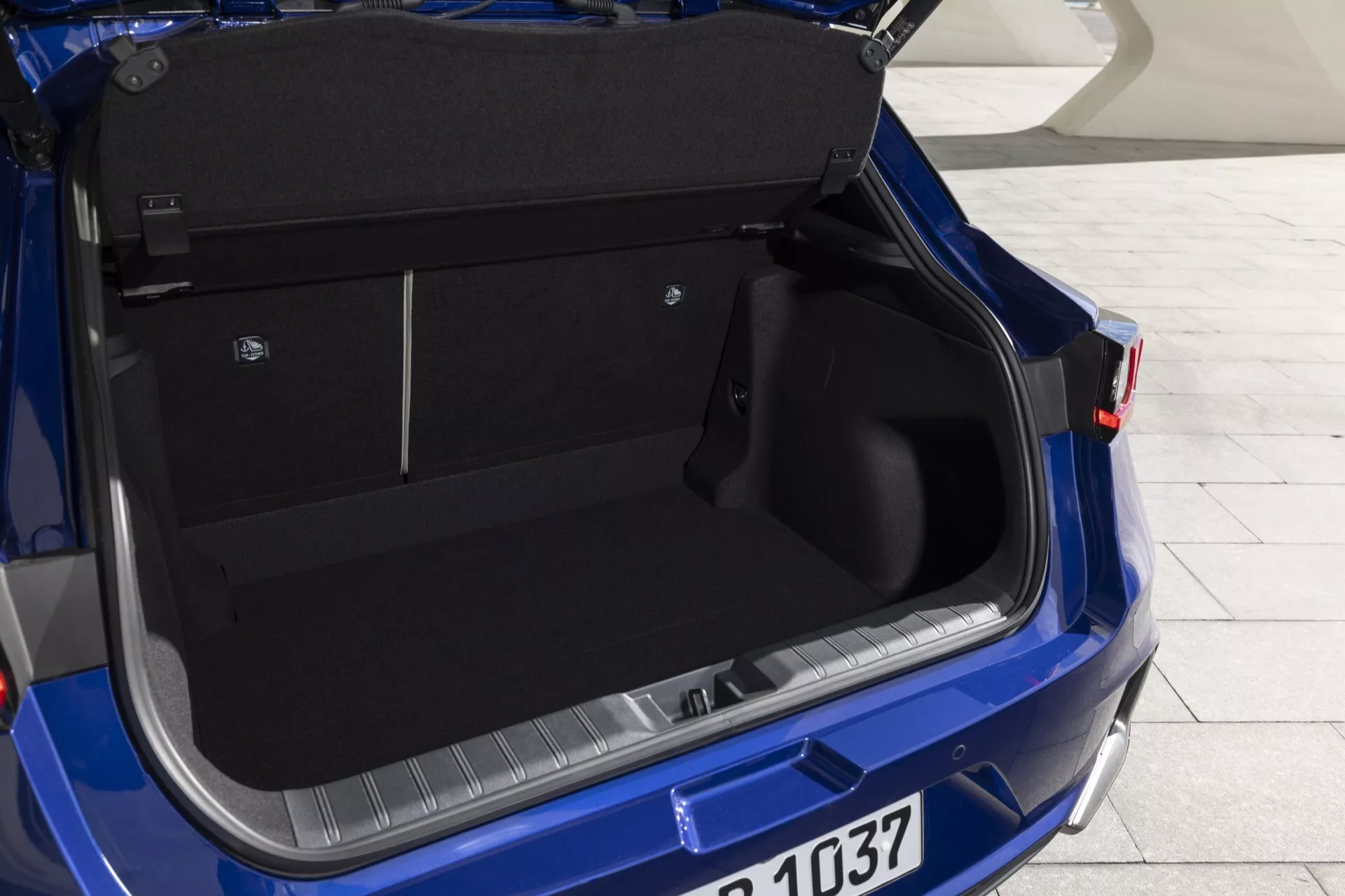 Vista ravvicinata del bagagliaio aperto della Lexus LBX 2024 con interni spaziosi e tappezzeria scura con meccanismo manuale del coperchio, con visibilità dettagliata della disposizione pulita dell'area di carico, partizione per l'organizzazione e sezione del paraurti posteriore con protezione, alla luce naturale del giorno