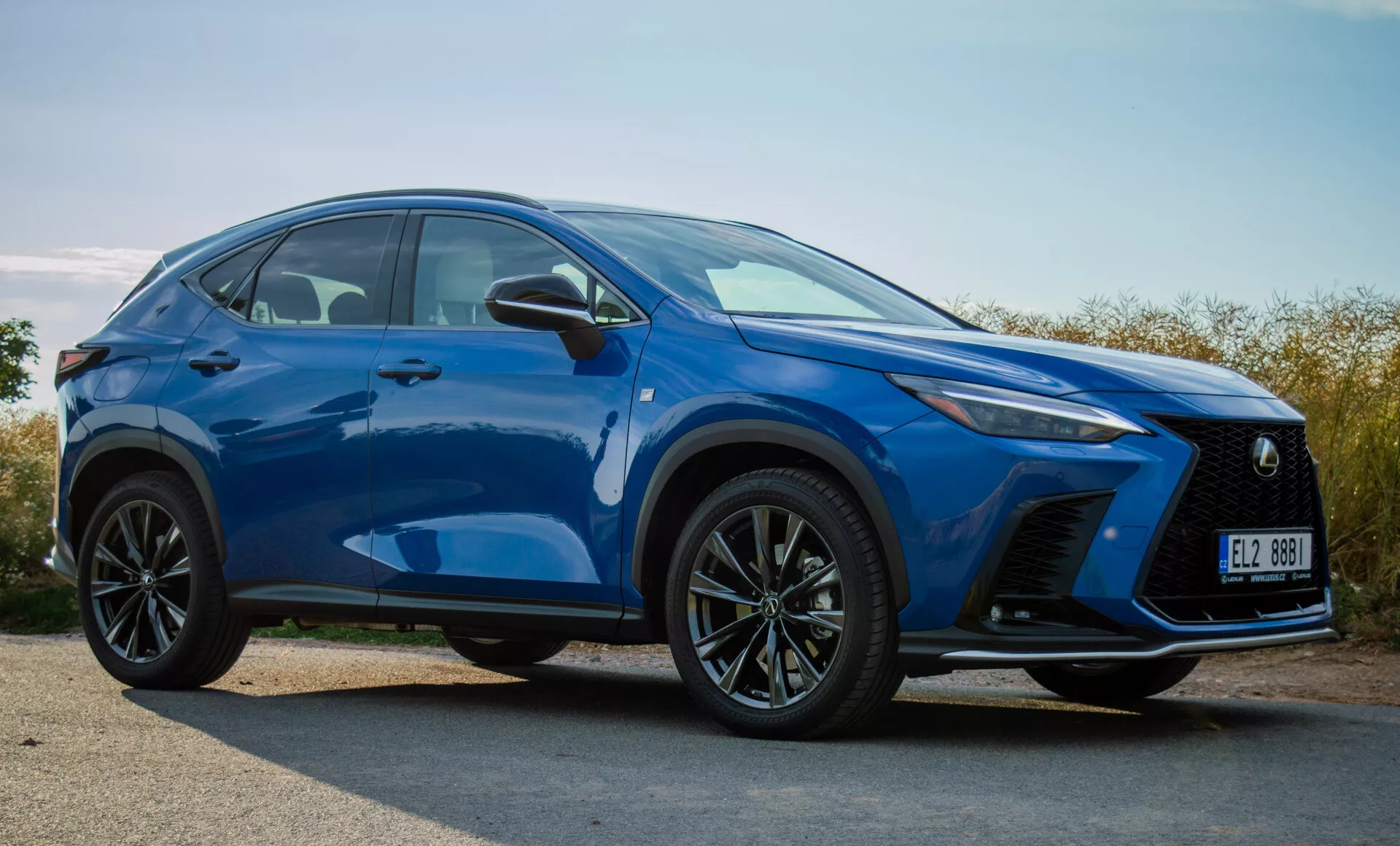 SUV compatto Lexus NX 2021 in blu vivace, mostrando paraurti anteriore, griglia, fari LED, cofano, ruote e linee del contorno laterale da un'angolazione frontale di tre quarti all'aperto alla luce del giorno