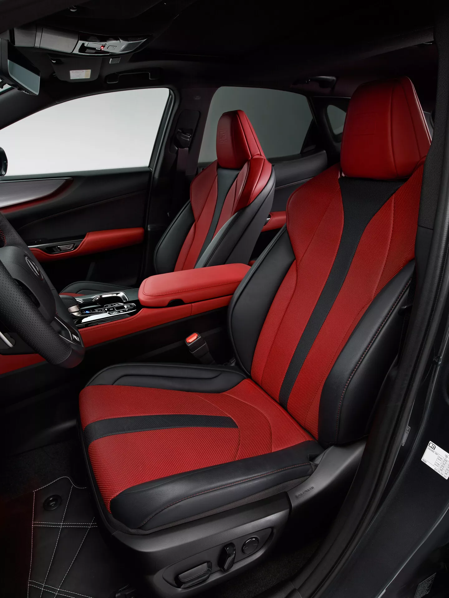 Foto degli interni di una Lexus NX 2021 che mostra l'area del passeggero anteriore dall'angolo del lato del guidatore. L'immagine mette in risalto il sedile del passeggero con tappezzeria rossa audace e dettagli neri, con un design sportivo con imbottiture migliorate e controlli regolabili elettricamente. La pannelleria della porta corrisponde allo schema di colori nero e rosso, con pelle, tessuto, una tasca portaoggetti, una griglia per altoparlante e vari comandi. Il consolle centrale mostra una leva del cambio automatica e un bracciolo centrale con cuciture rosse, riflettendo il design lussuoso e sportivo del veicolo.