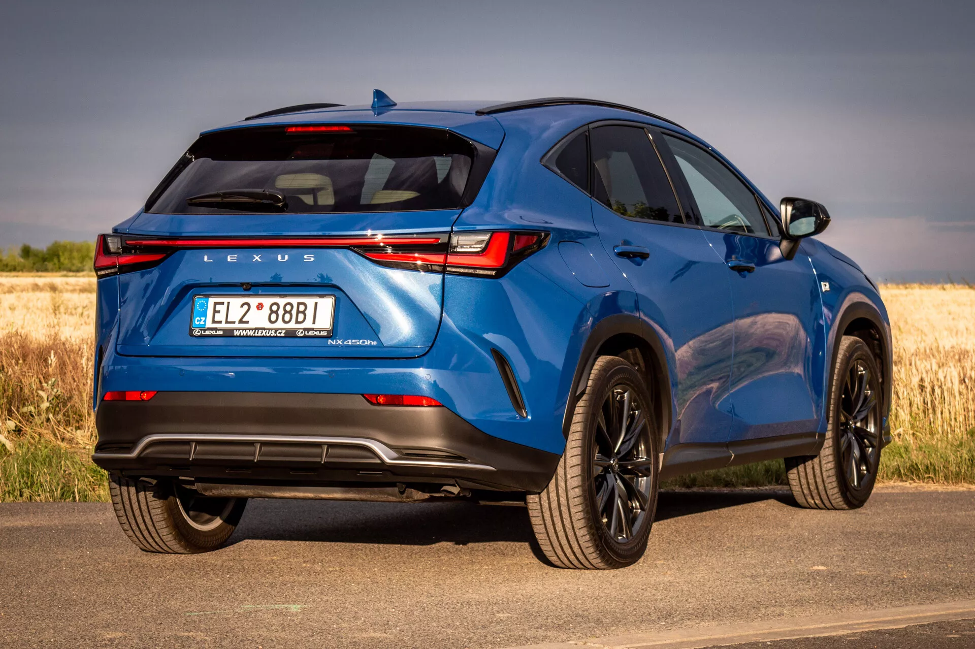 SUV Lexus NX blu 2021 in vista posteriore a tre quarti che mostra elementi di design e caratteristiche tecnologiche in una giornata di sole con sfondo naturale