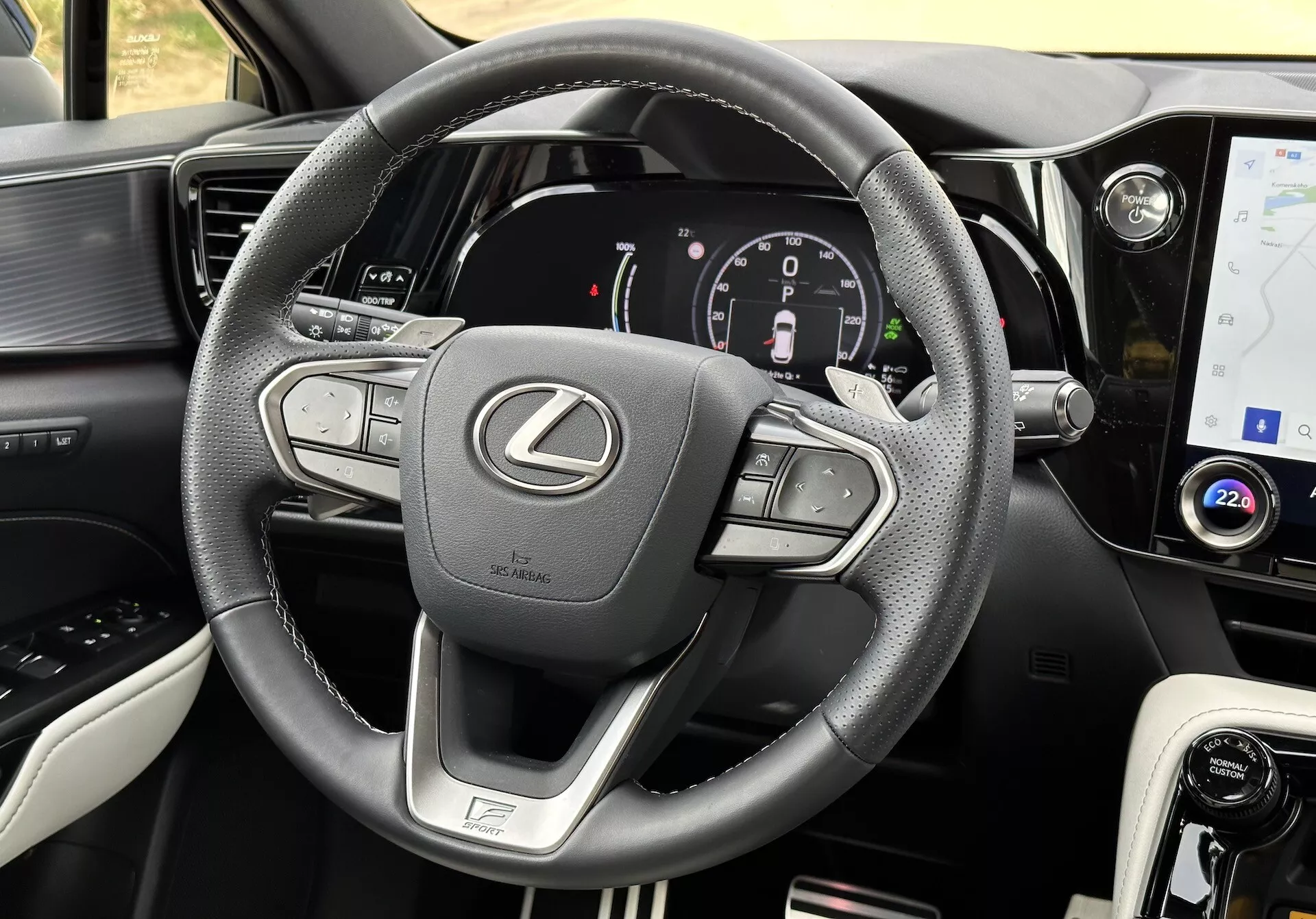 Vista interna di una Lexus NX 2021 con focus sul volante e cruscotto, che mostra pulsanti multifunzione, un cluster strumenti digitale, touchscreen per infotainment, accentature in pelle, selettore modalità di guida, bocchette d'aria e cuciture dettagliate.