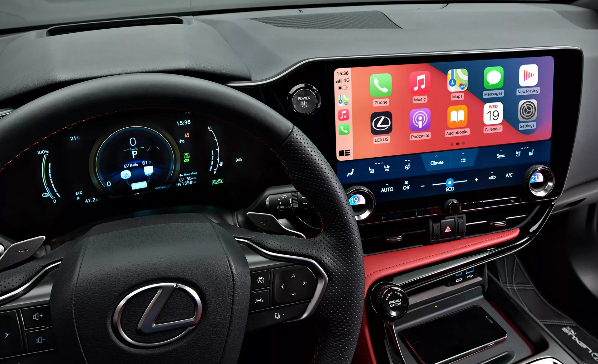 Vista interna di una Lexus NX 2021 che mostra un cruscotto moderno e tecnologicamente avanzato dalla prospettiva del conducente. A sinistra è visibile parzialmente il volante con il logo Lexus e pulsanti multifunzione. Il quadro strumenti digitale mostra velocità, giri al minuto e altre metriche in blu e bianco. Al centro, il prominente ampio schermo touchscreen del sistema di infotainment integra le funzionalità degli smartphone. Sotto ci sono i pulsanti e le manopole di controllo del clima con display digitali della temperatura. La sezione inferiore include una console cucita in pelle con la leva del cambio e porte di connettività, riflettendo le finiture lussuose del veicolo.