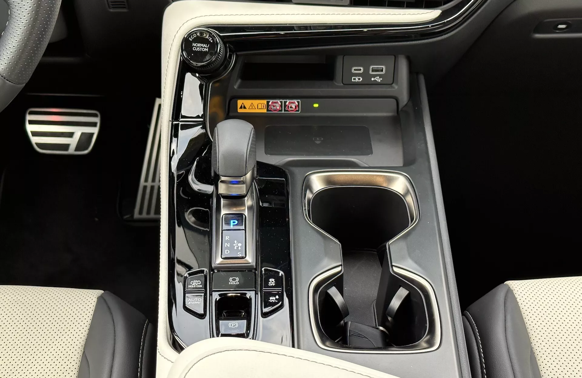 Vista della consolle centrale Lexus NX 2021 che mostra la leva del cambio automatico con cuffia in pelle, selettore della modalità di guida, portabicchieri, pulsanti di controllo del veicolo, potenziali scorciatoie per l'infotainment e elementi del design interno di lusso