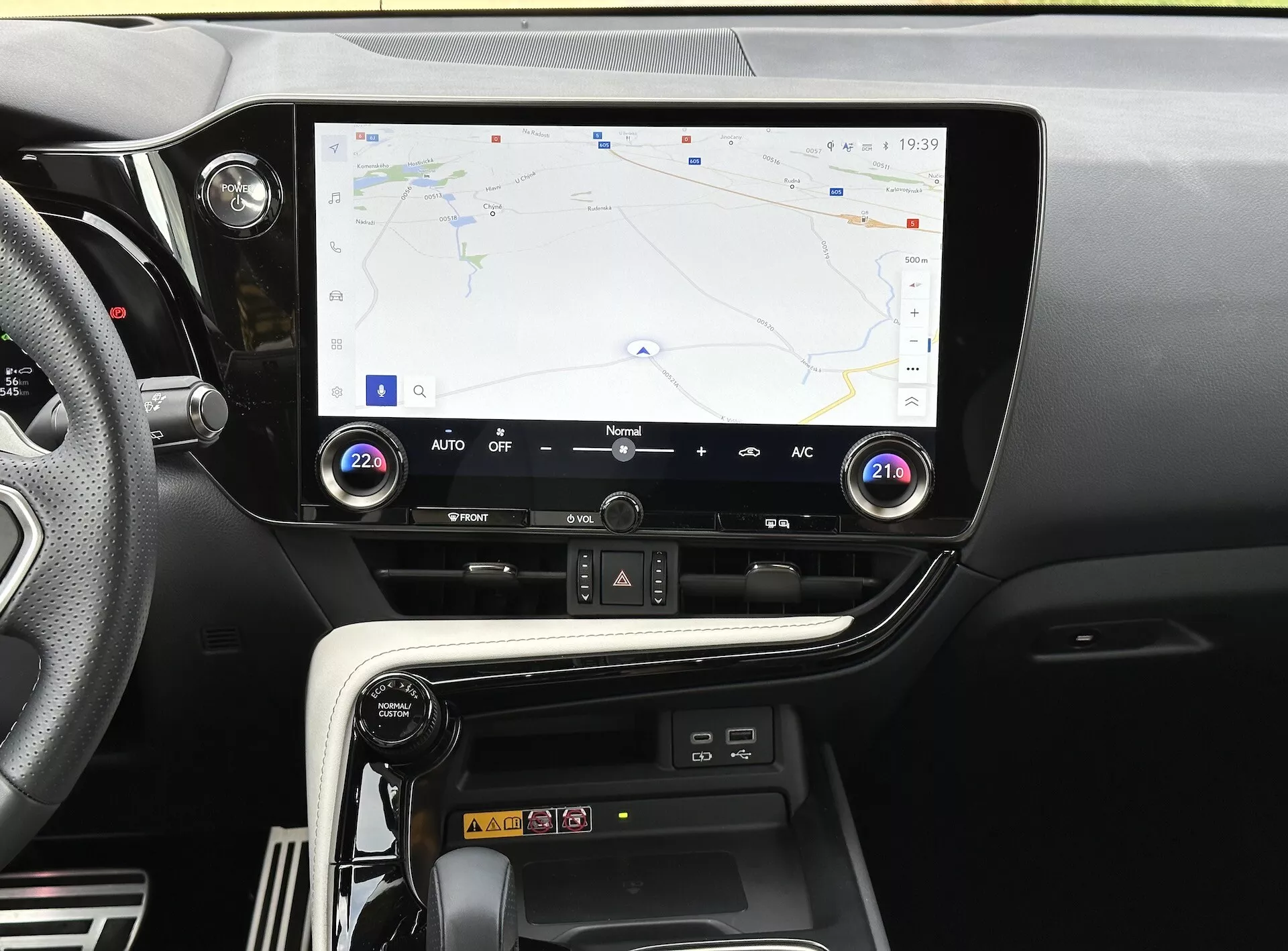 Console centrale del Lexus NX 2021 con display touchscreen che mostra navigazione GPS, pulsanti e manopole per il controllo del clima e scomparto per la ricarica dello smartphone