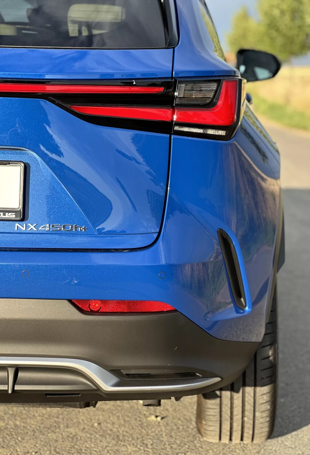 Vista angolare ravvicinata della sezione posteriore di un SUV crossover ibrido Lexus NX 450h+ blu, con particolare attenzione alla finitura lucida, fanali posteriori LED, distintivo ibrido e caratteristiche di design sportivo
